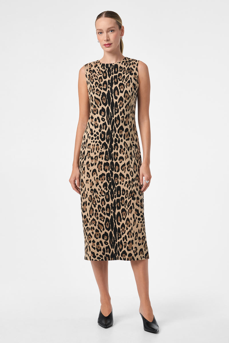 A woman poses against a white background wearing the Dame Dress, a sleeveless, knee-length, form-fitting piece featuring a bold brown and black leopard print. She completes the look with black heels.