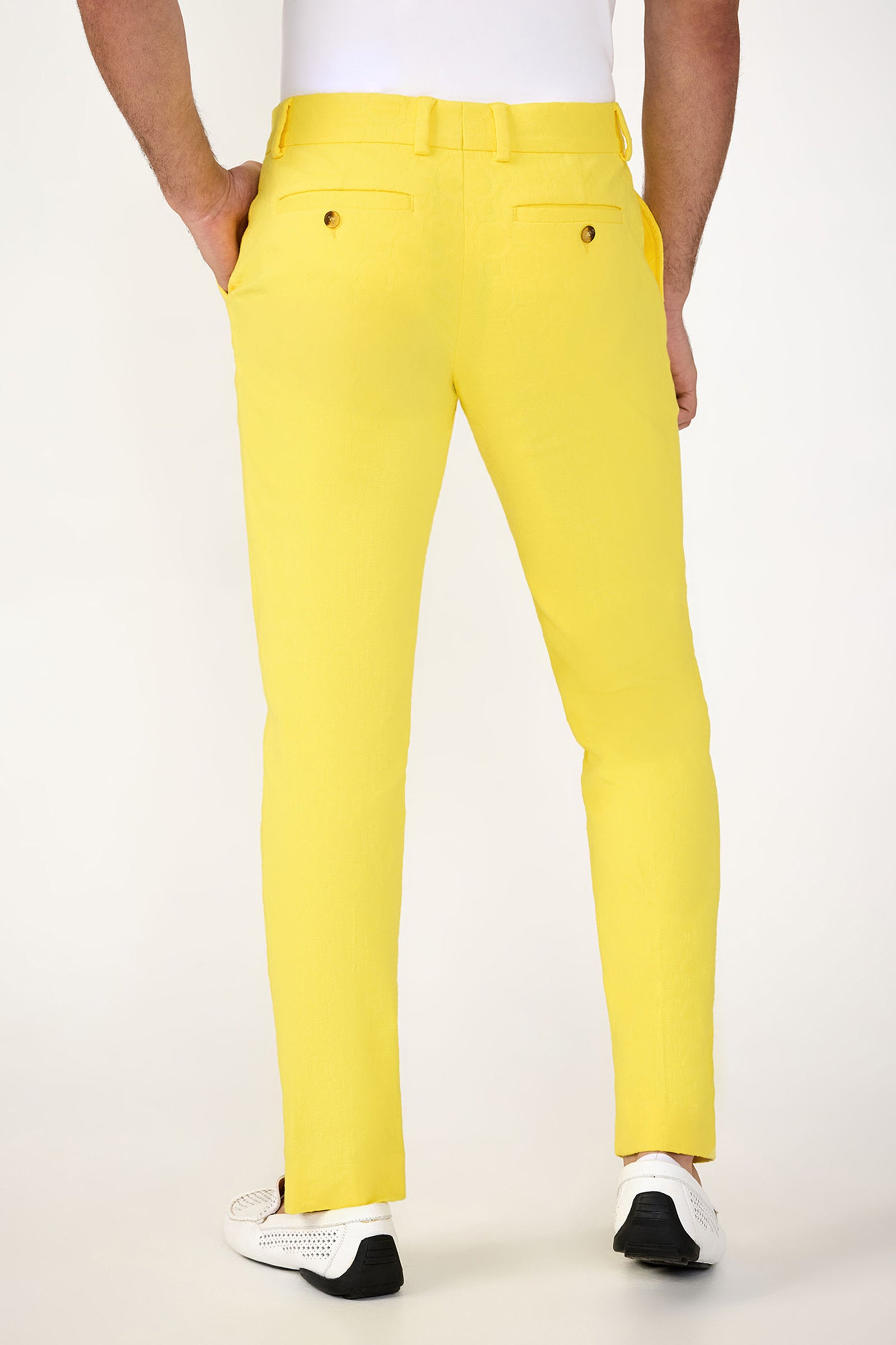 A man wearing the Clyde Slim Trouser - Stretch Herringbone in bright yellow and white sneakers stands with hands in pockets, facing away from the camera against a plain white background.