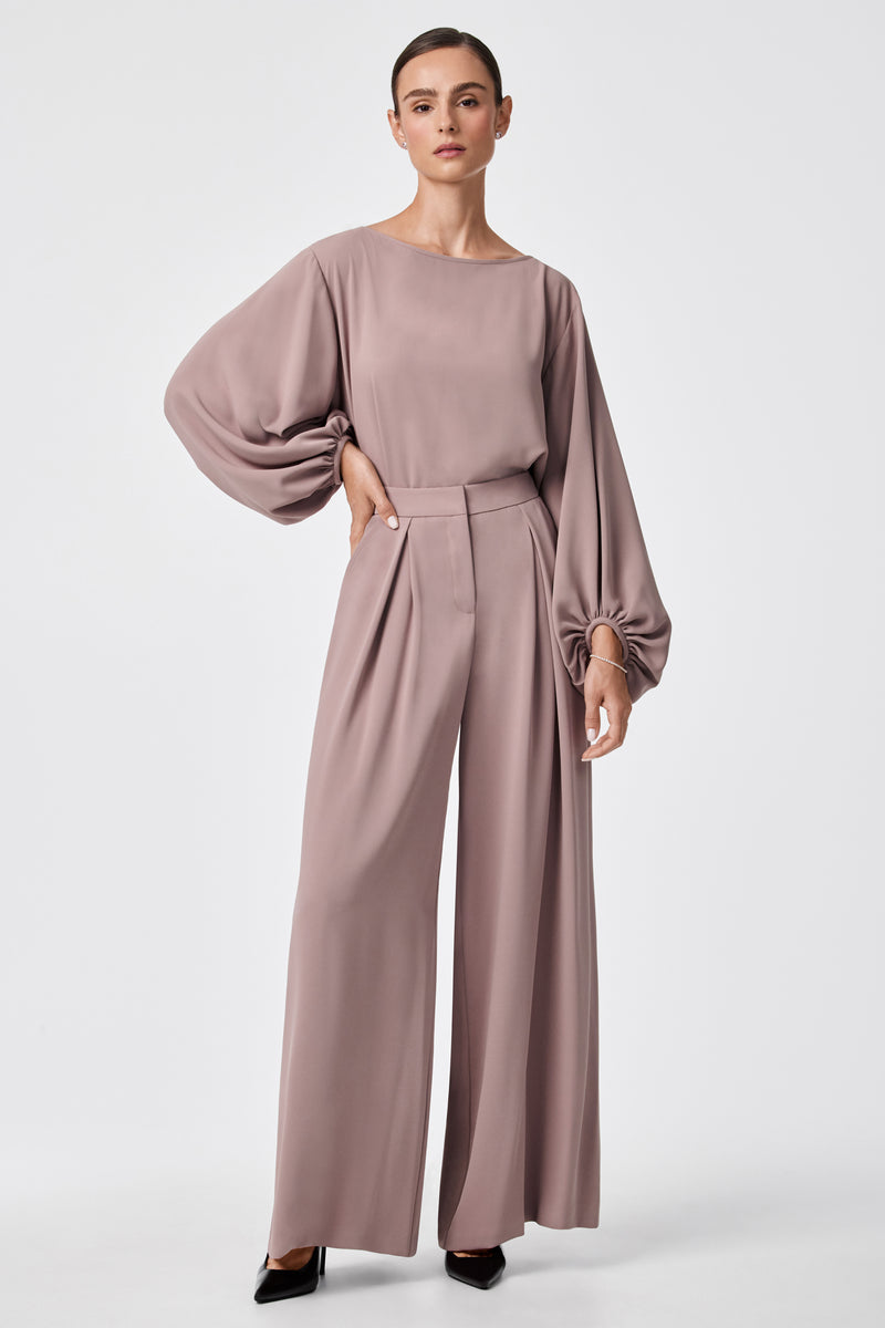 A woman wears Saige Wide-Leg Short Pants in mauve with a matching billowy long-sleeve blouse and black pointed-toe heels, standing against a plain white background.