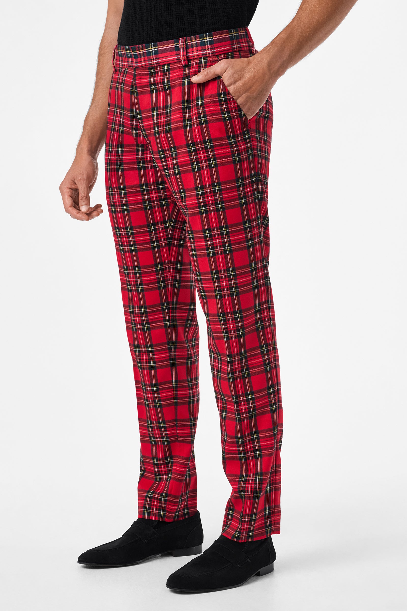 A person wearing Clyde Slim Trouser - Can-Can Check, featuring red plaid with black, yellow, and green lines, paired with a black top and black shoes, stands with one hand in their pocket against a white background.