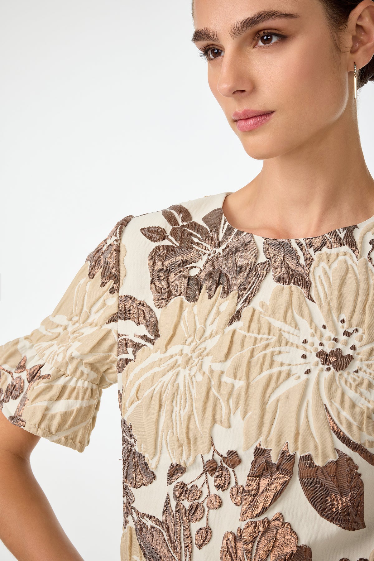 A woman wearing the Darling Flounce Sleeve Dress, featuring a cream color with large brown and beige floral patterns, stands against a plain background, gazing slightly to the side with a neutral expression.
