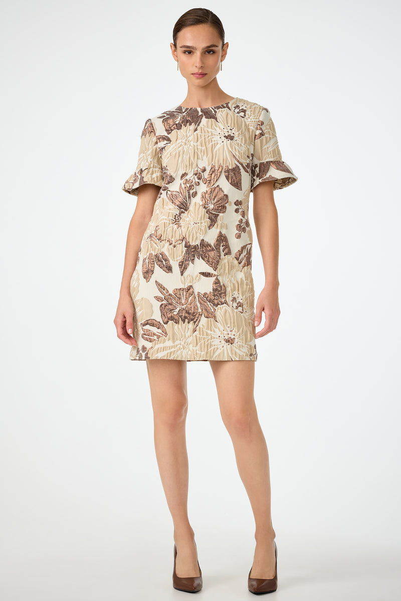 A woman stands facing forward against a white background, wearing the Darling Flounce Sleeve Dress in Daintree Jacquard with ruffled short sleeves and brown heels. Her brown hair is pulled back.