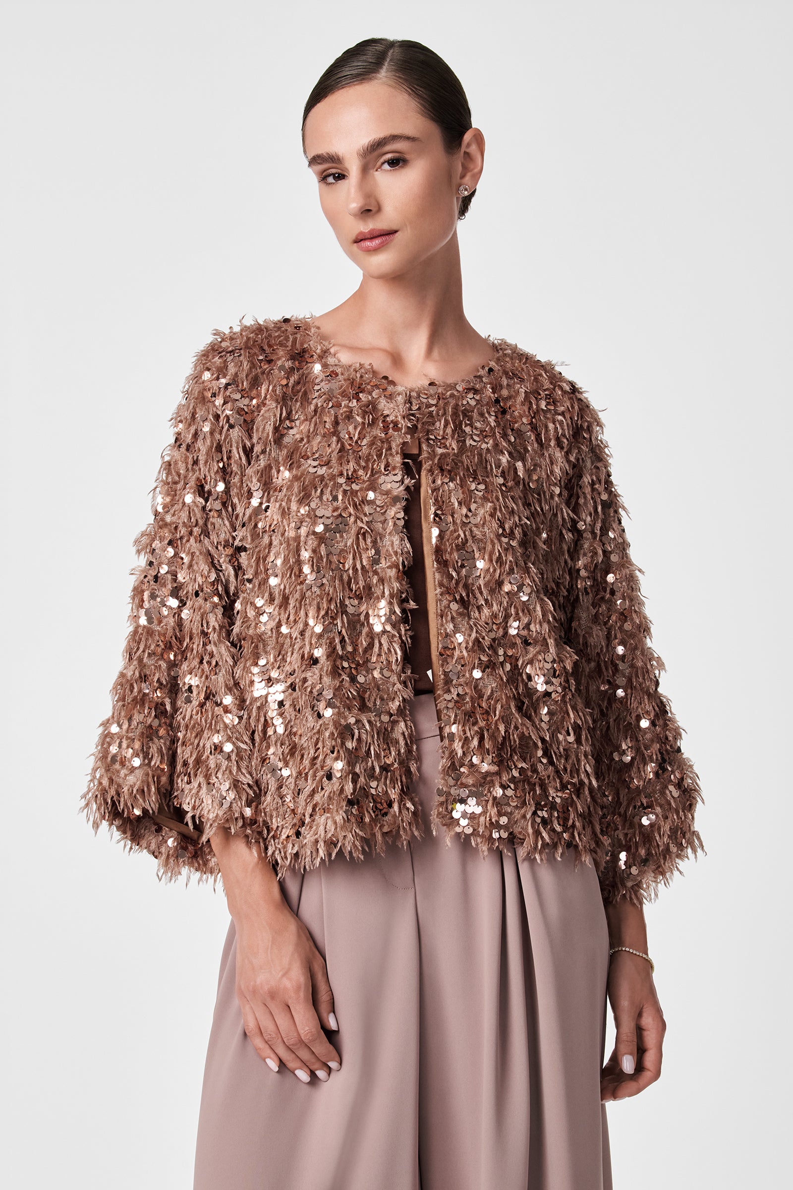 A woman wears the Fete Faux Fur Stole over matching pleated high-waisted trousers, standing against a plain light background with her hair pulled back and a confident, neutral expression.