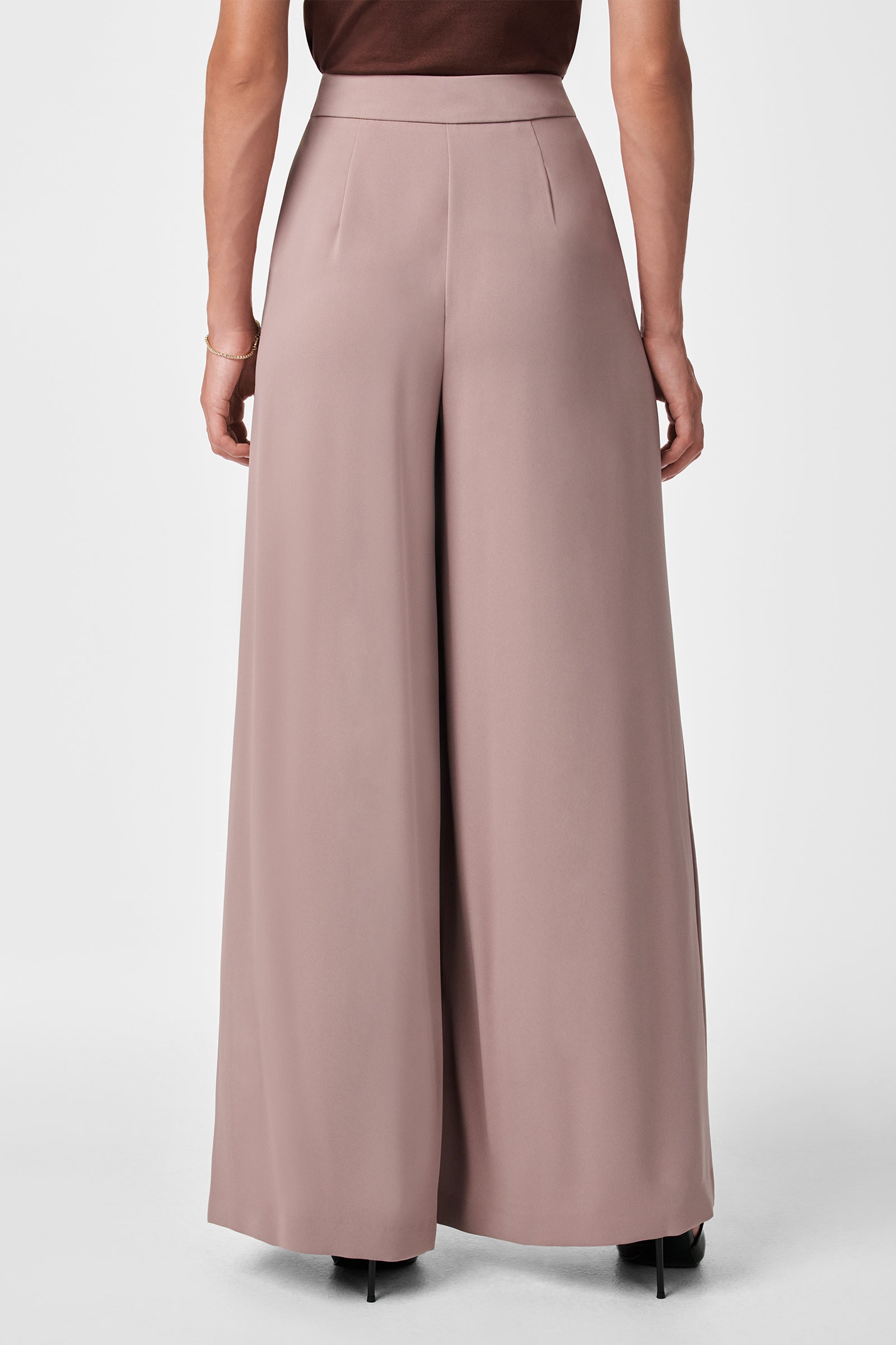 A person is shown from the back wearing blush pink Saige Wide-Leg Pants with a sleeveless brown top and black heeled shoes, standing against a plain background.