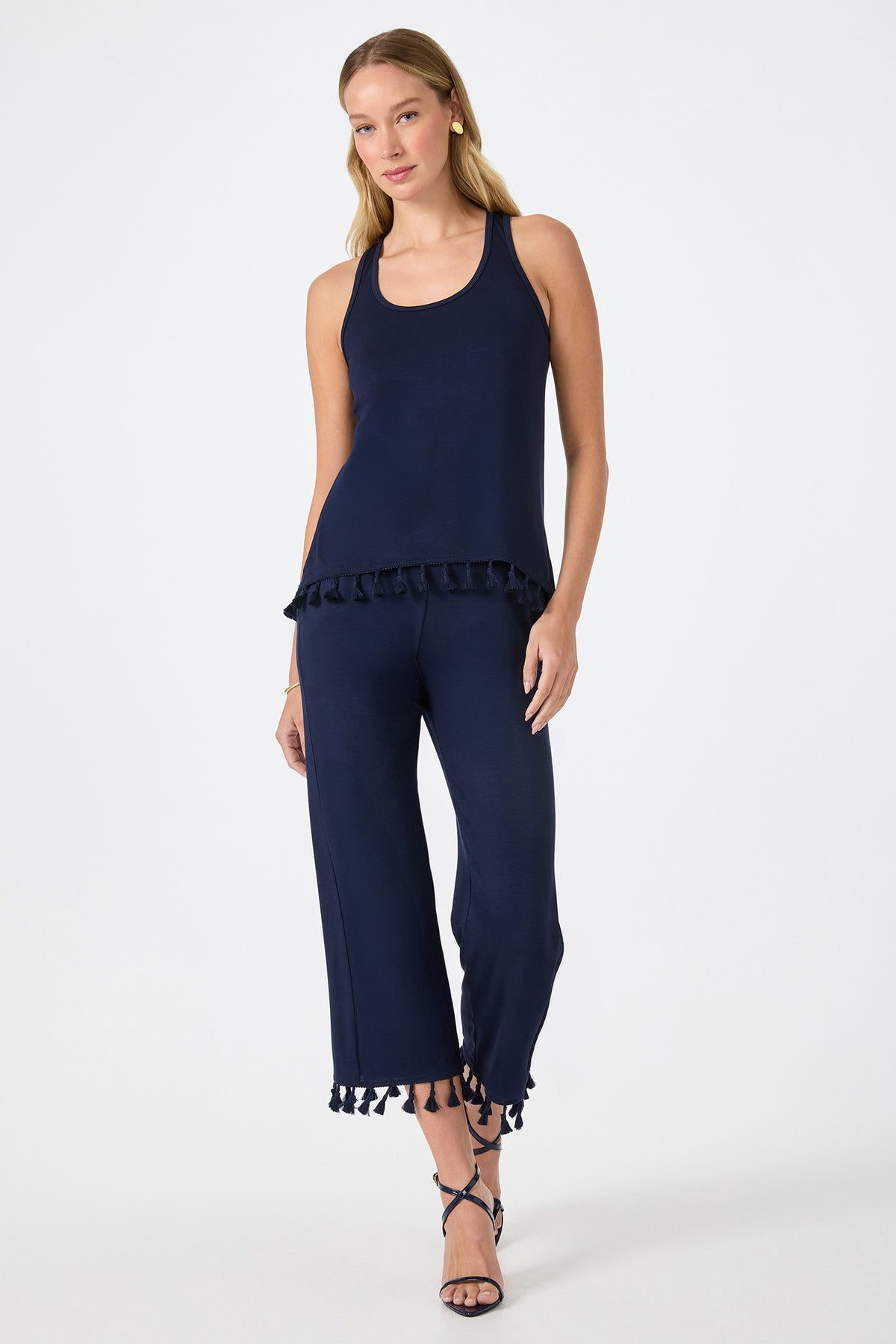 A woman wears the Tajo 2 Tassel Hem Sleeveless Top in navy blue with matching wide-leg pants and strappy sandals, standing against a plain white background.
