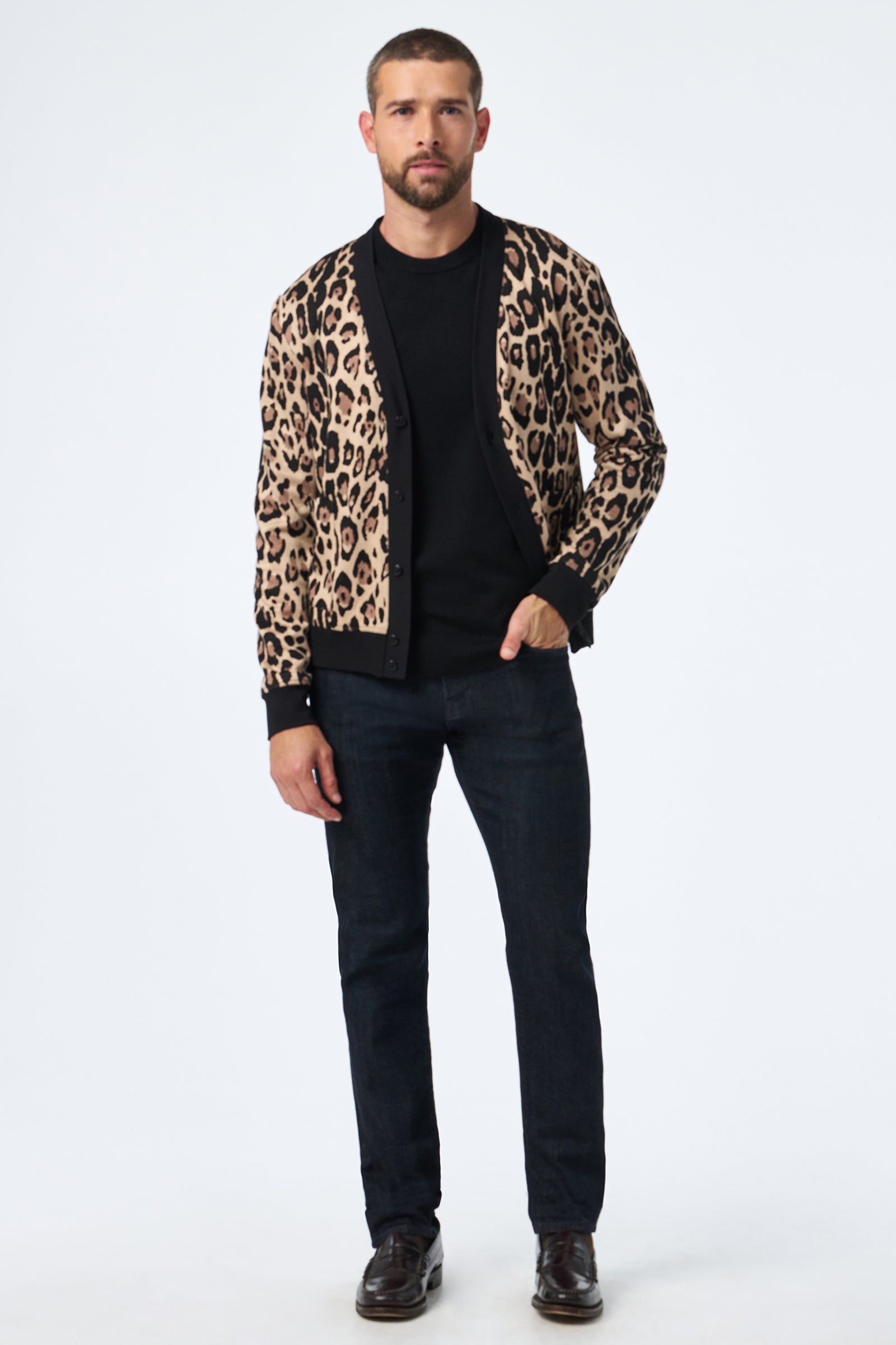 A man faces forward against a plain white background, wearing the Darryl Knit Cardigan, which features a tan and black leopard print over a black shirt, dark jeans, and dark shoes.