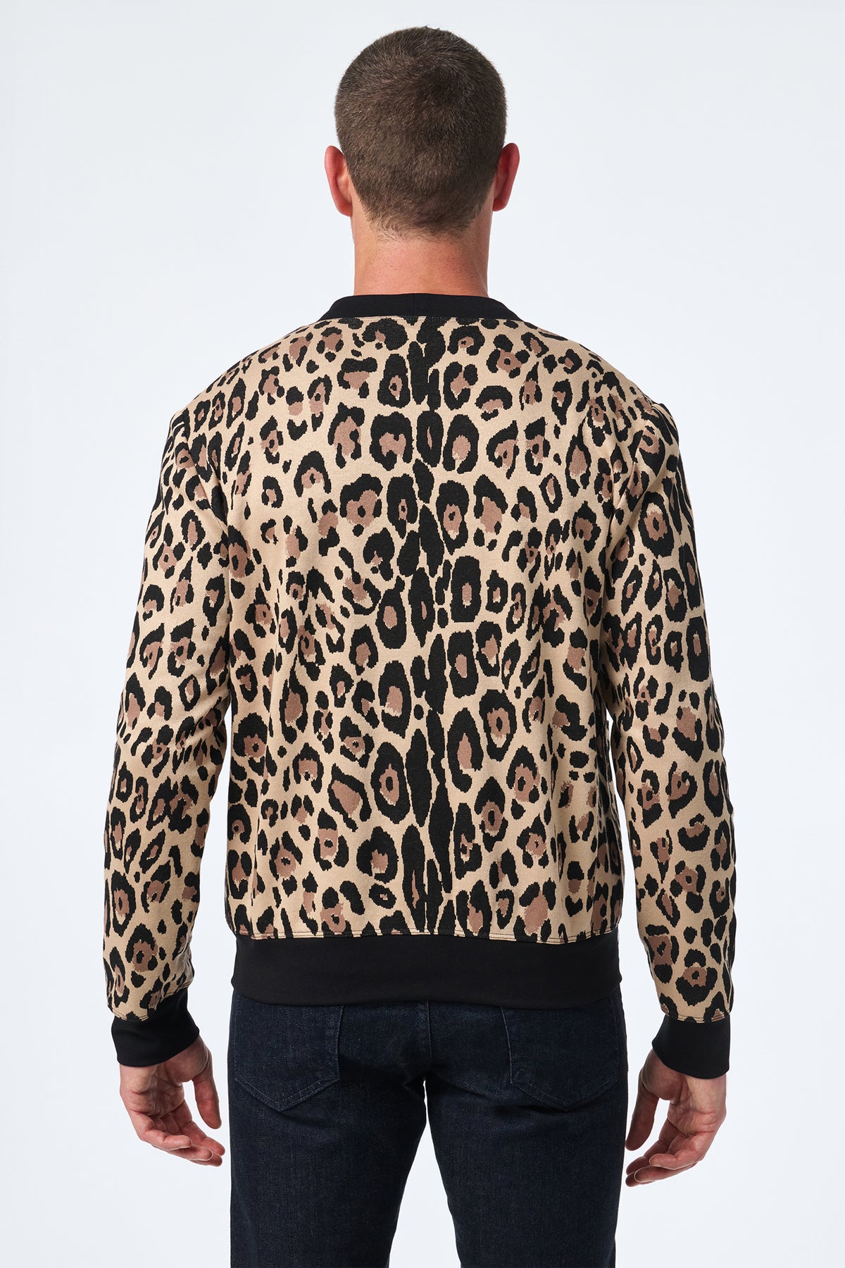 A man with short hair, seen from the back, wears the Darryl Knit Cardigan—a long-sleeve leopard print cardigan featuring black trim at the cuffs and hem—while standing against a plain white background.