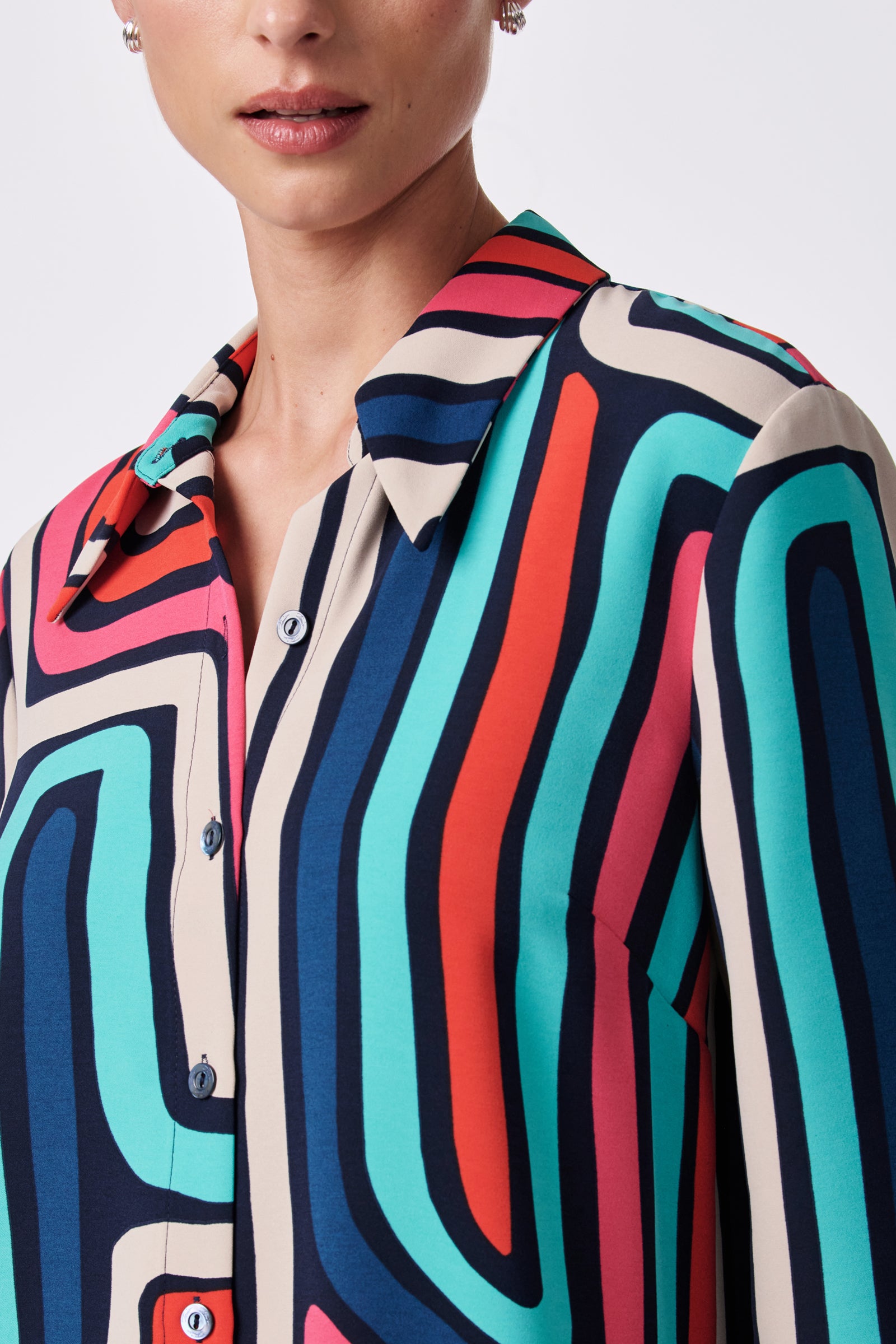 A woman wears the Montero Top—a colorful button-up with bold, abstract wavy patterns in blue, teal, red, navy, and cream. Only her lower face and upper torso are visible against a plain background.