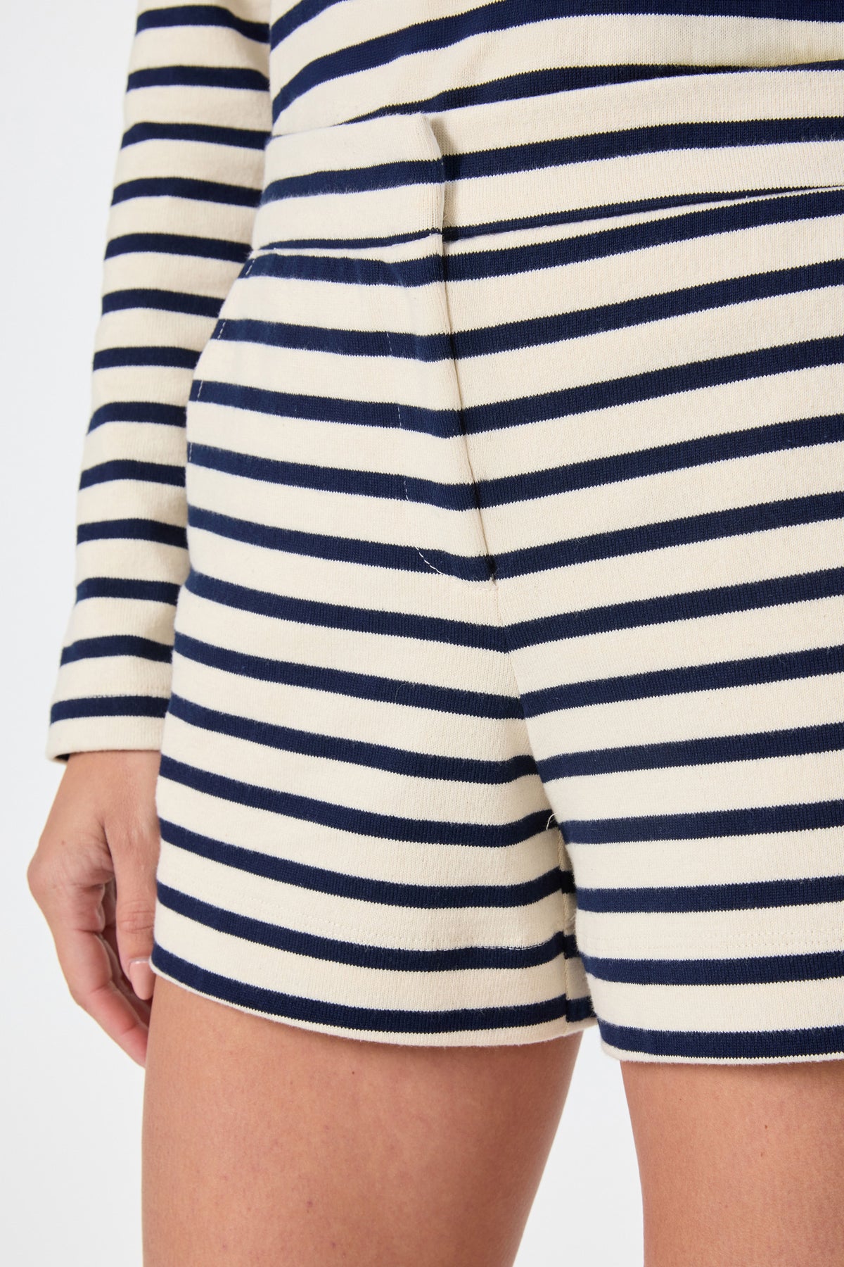 Close-up of a person wearing the Corbin 2 Shorts in Noh Nightfall Stripe with a matching long-sleeve top in cream and navy stripes. Their left hand is relaxed by their side.