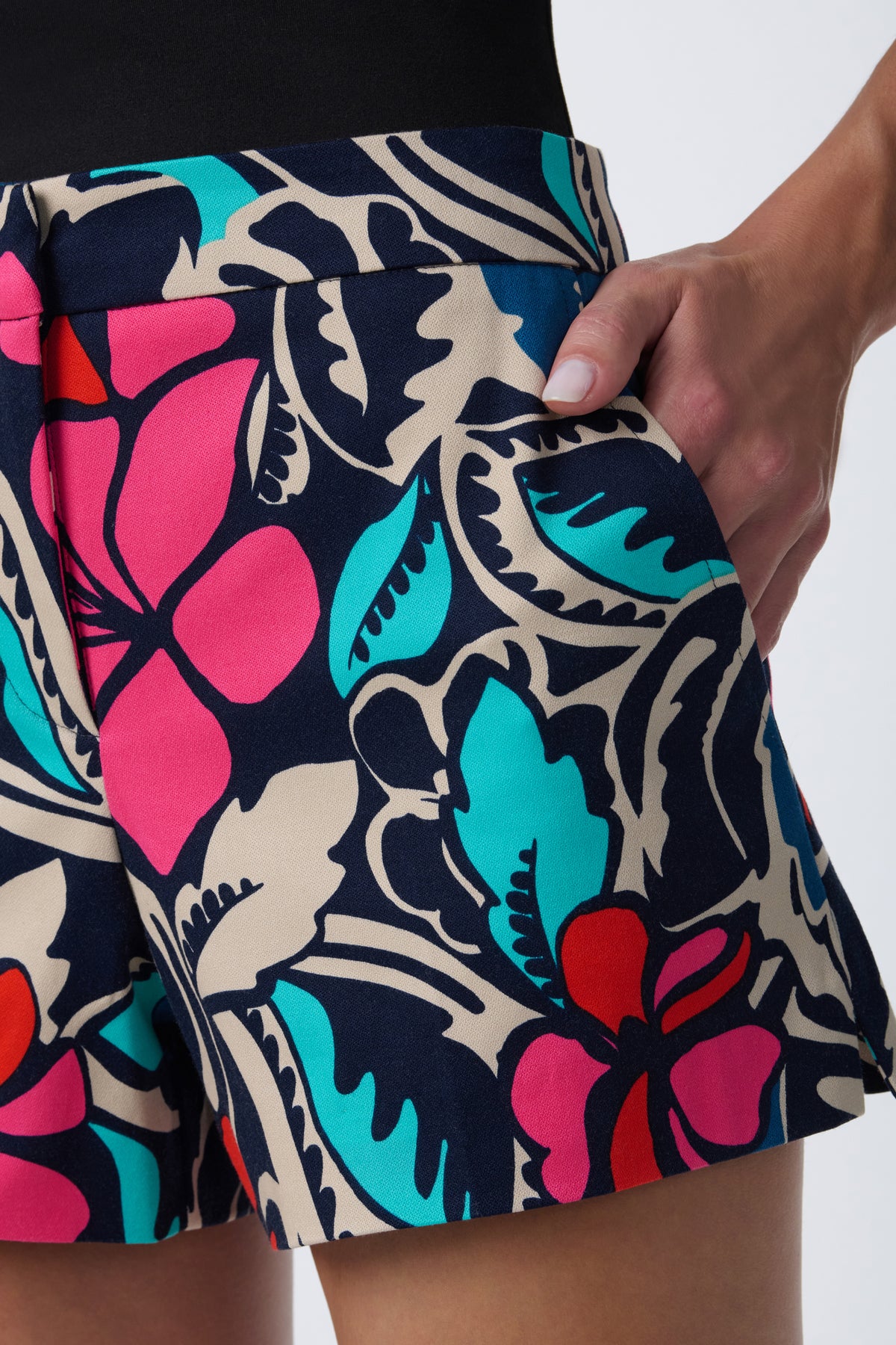 A person wearing the Corbin 2 Short, featuring a bold floral print in pink, teal, red, and navy, stands with one hand in their pocket against a plain light background.
