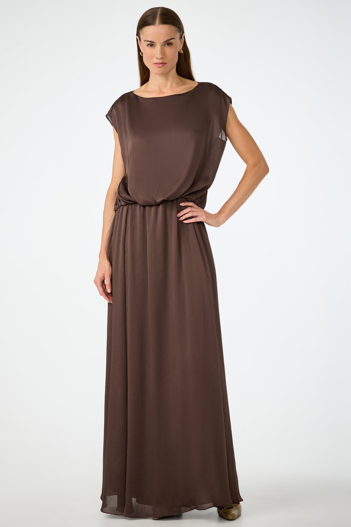 A woman poses confidently against a plain background, wearing the Vantage 2 Maxi Dress in Walnut—a sleeveless, loose-fitting design with a cinched waist. She has straight hair and rests one hand on her hip.