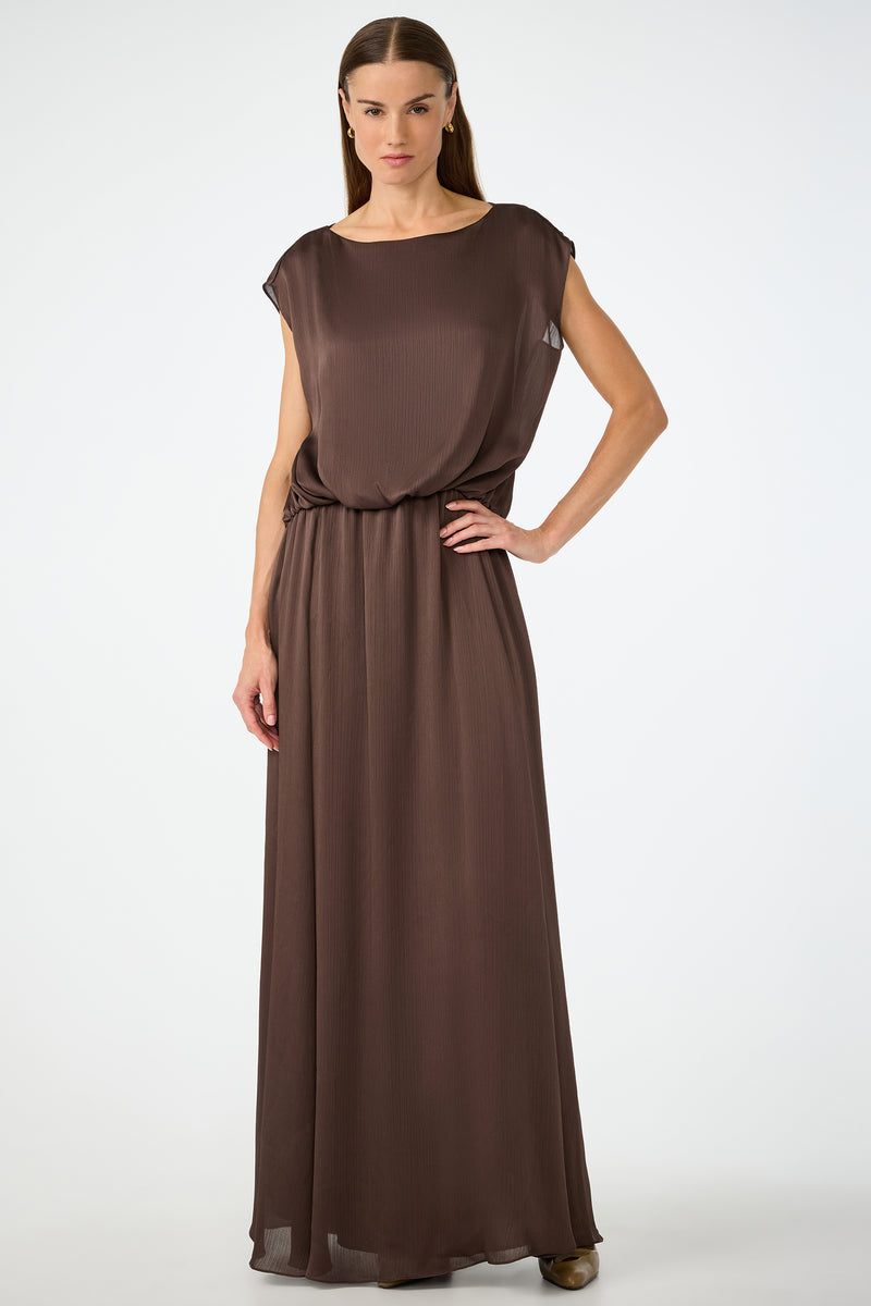 A woman poses confidently against a plain background, wearing the Vantage 2 Maxi Dress in Walnut—a sleeveless, loose-fitting design with a cinched waist. She has straight hair and rests one hand on her hip.
