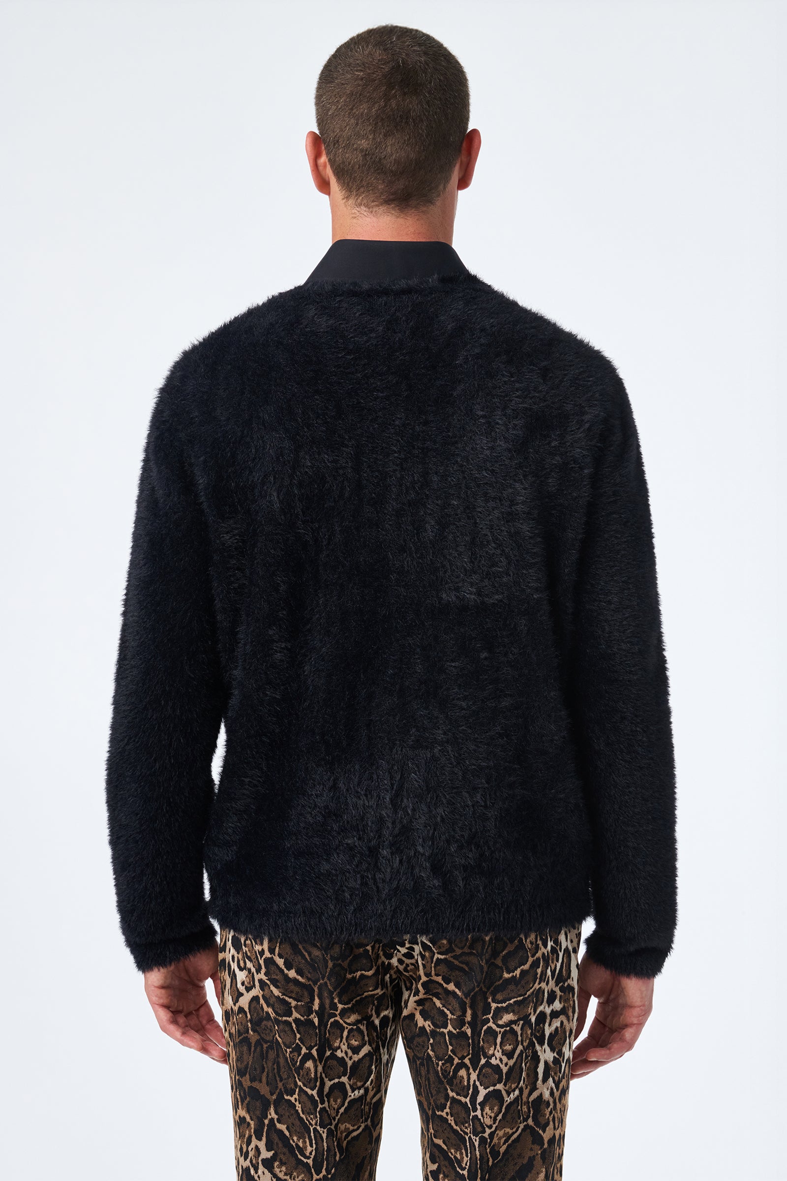 A person stands with their back to the camera, wearing the Scott Fuzzy Cardigan in black and brown animal-print pants against a plain, light-colored background.