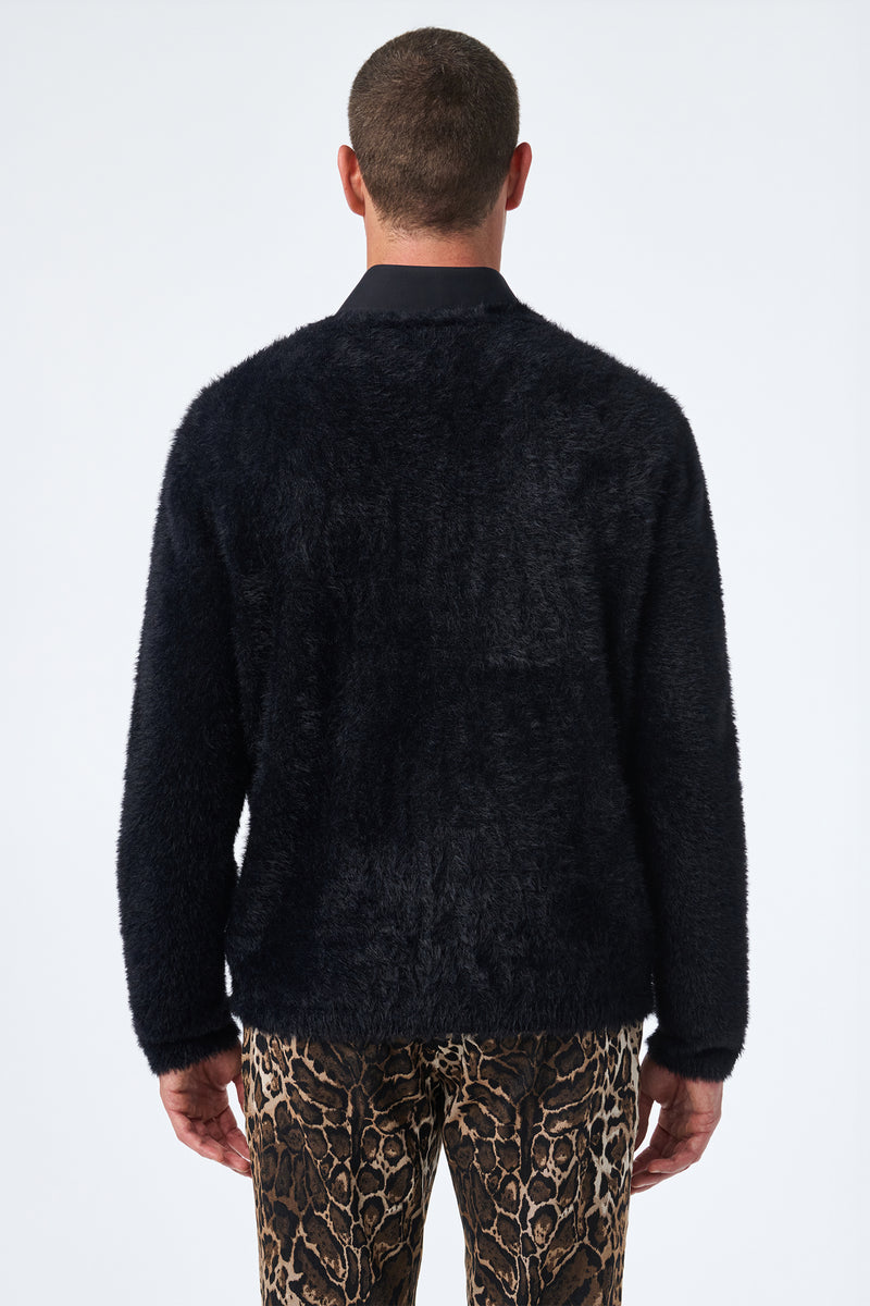A person stands with their back to the camera, wearing the Scott Fuzzy Cardigan in black and brown animal-print pants against a plain, light-colored background.