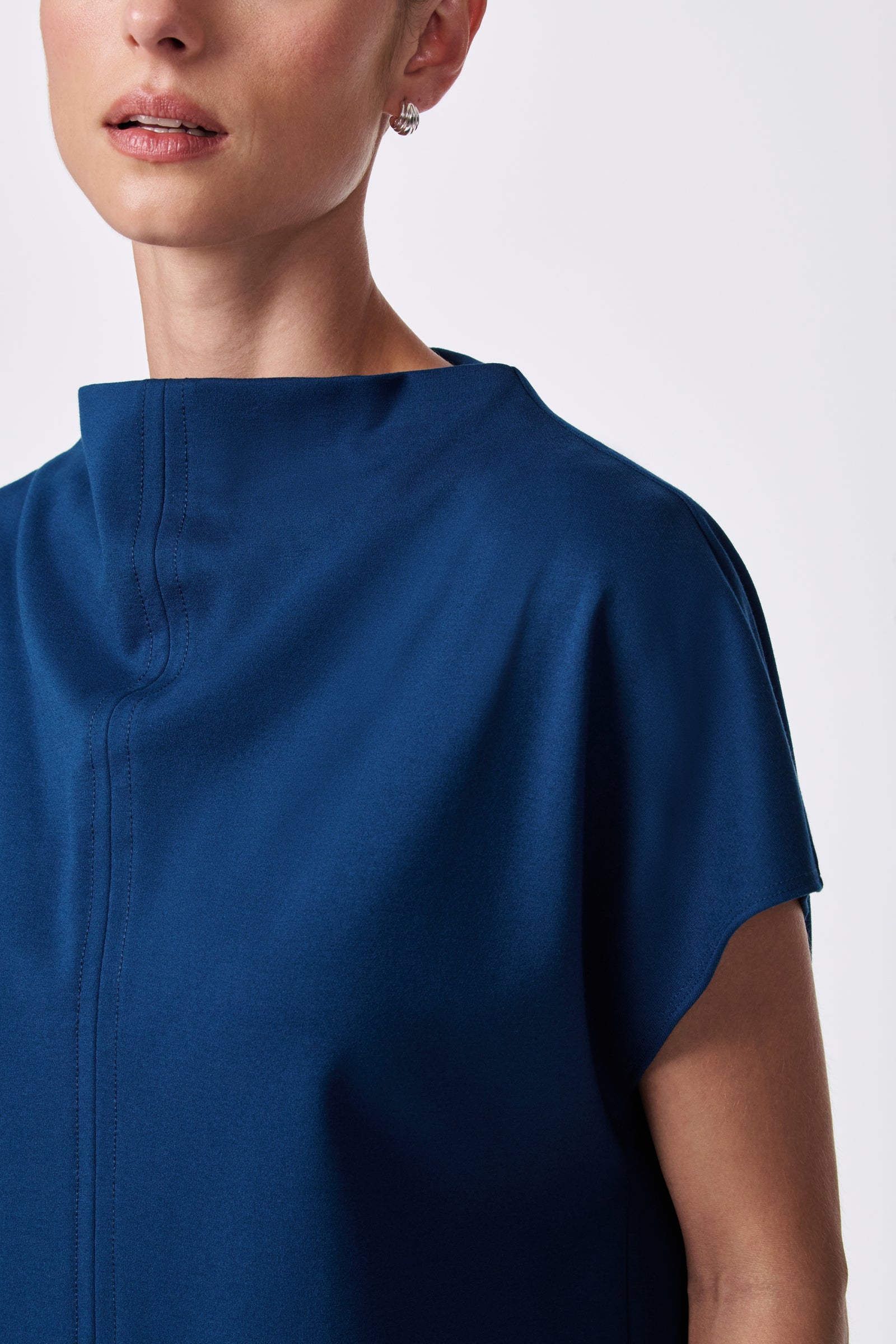 A woman wears the Pavilion Top—a dark blue, short-sleeve, high-collared blouse. Only her lower face, neck, and part of her upper body are shown against a plain light background.