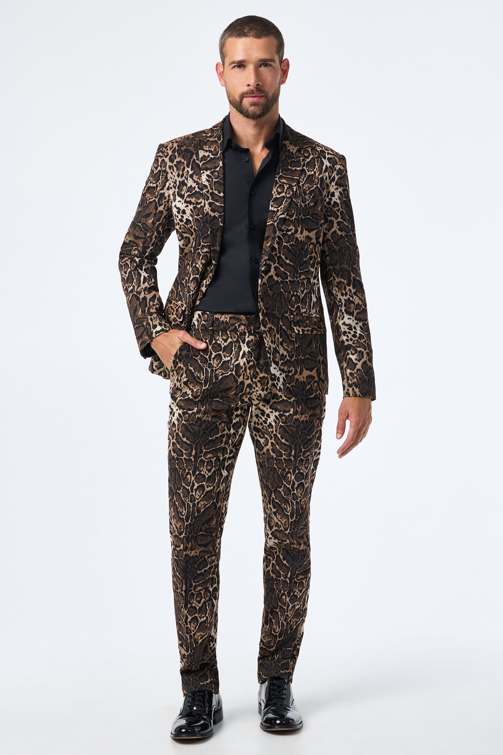 A man faces forward in Clyde Slim Trouser - Lompoul Leopard, paired with a black shirt and black dress shoes against a plain white background.