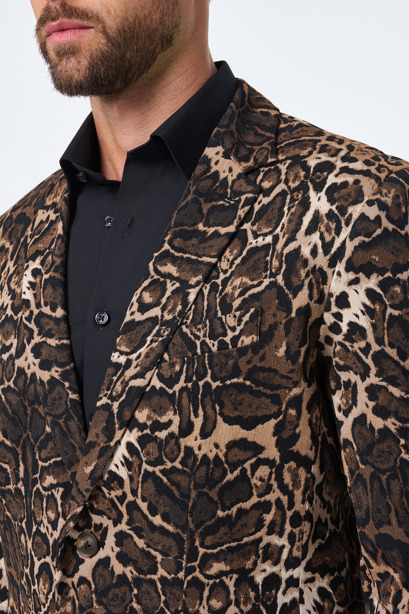 A man wearing the Thurston Blazer in Lompoul Leopard, featuring a brown and black leopard print, over a black dress shirt, shown from the shoulders up against a plain light background.