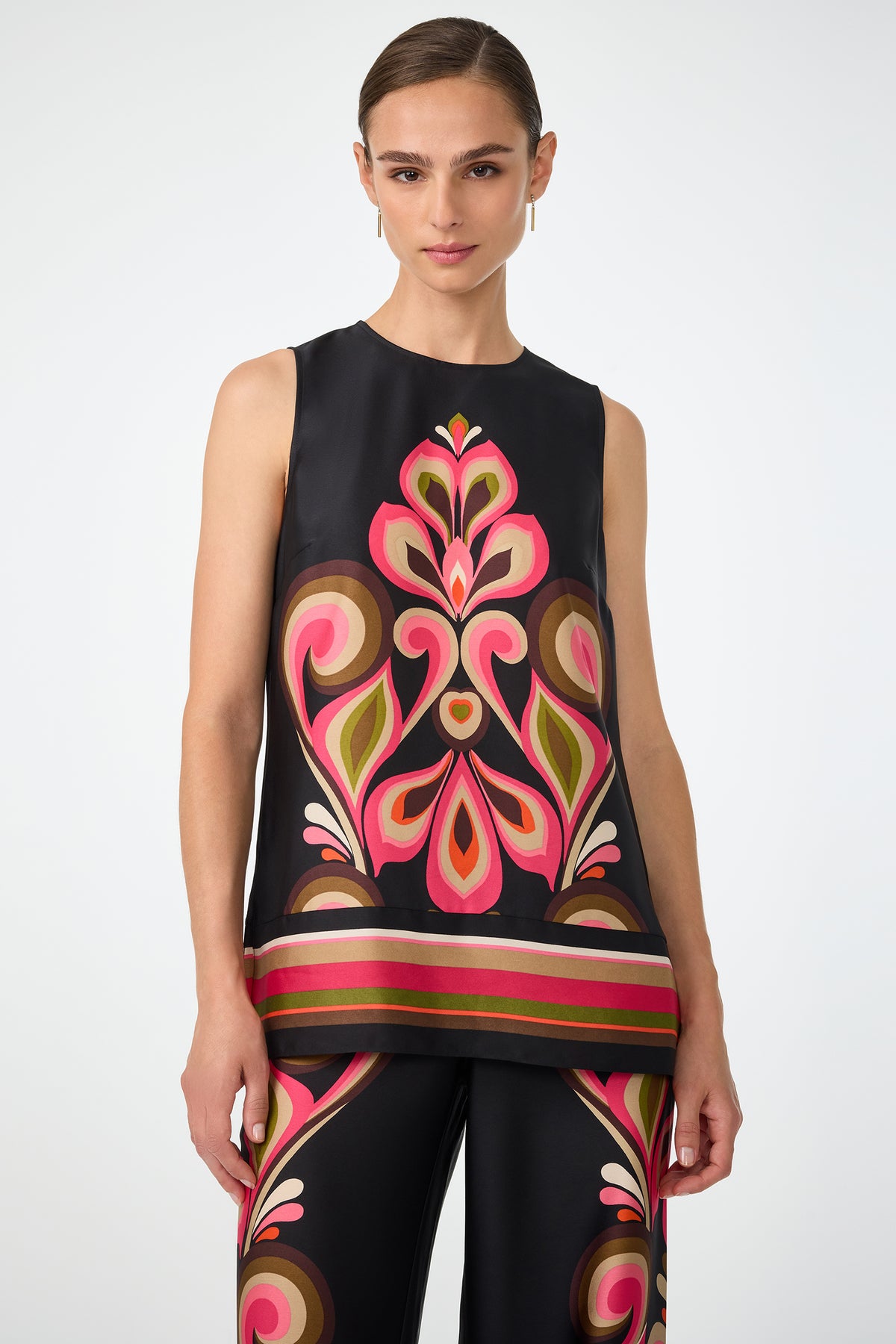 A woman wears the Malema Sleeveless Top in Sanctuary, paired with matching pants featuring vibrant geometric and floral patterns in pink, red, green, and tan. She is posed against a plain, light background.