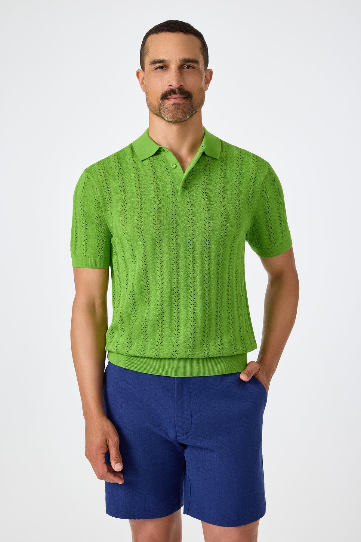 A man with short hair and a mustache wears the Cole Short-Sleeve Polo in Sogen Green and blue shorts, standing against a plain white background.