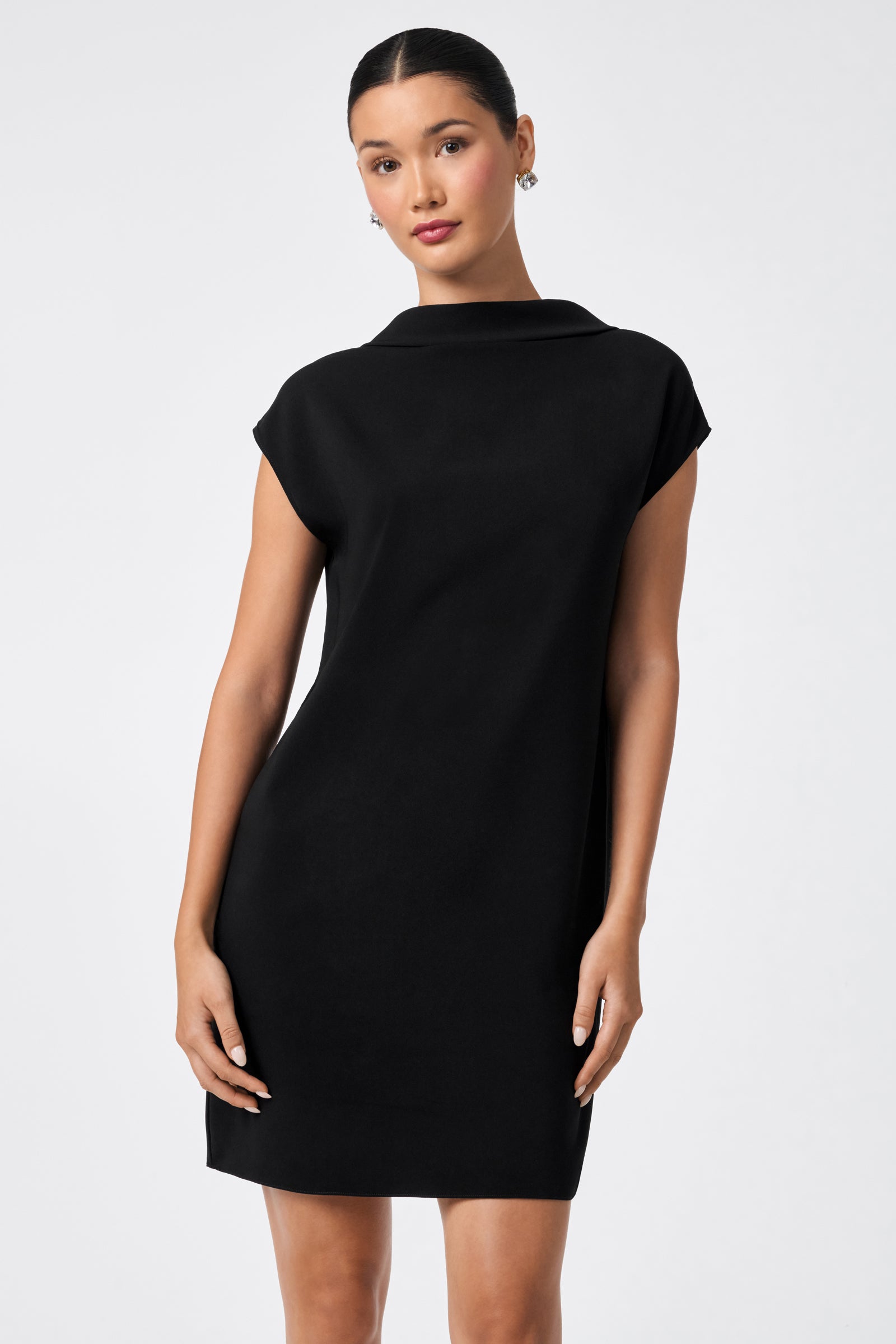 A woman faces backward in the CHORUS 2 DRESS—a black, collared, knee-length dress with short sleeves—looking over her shoulder at the camera against a plain light background.