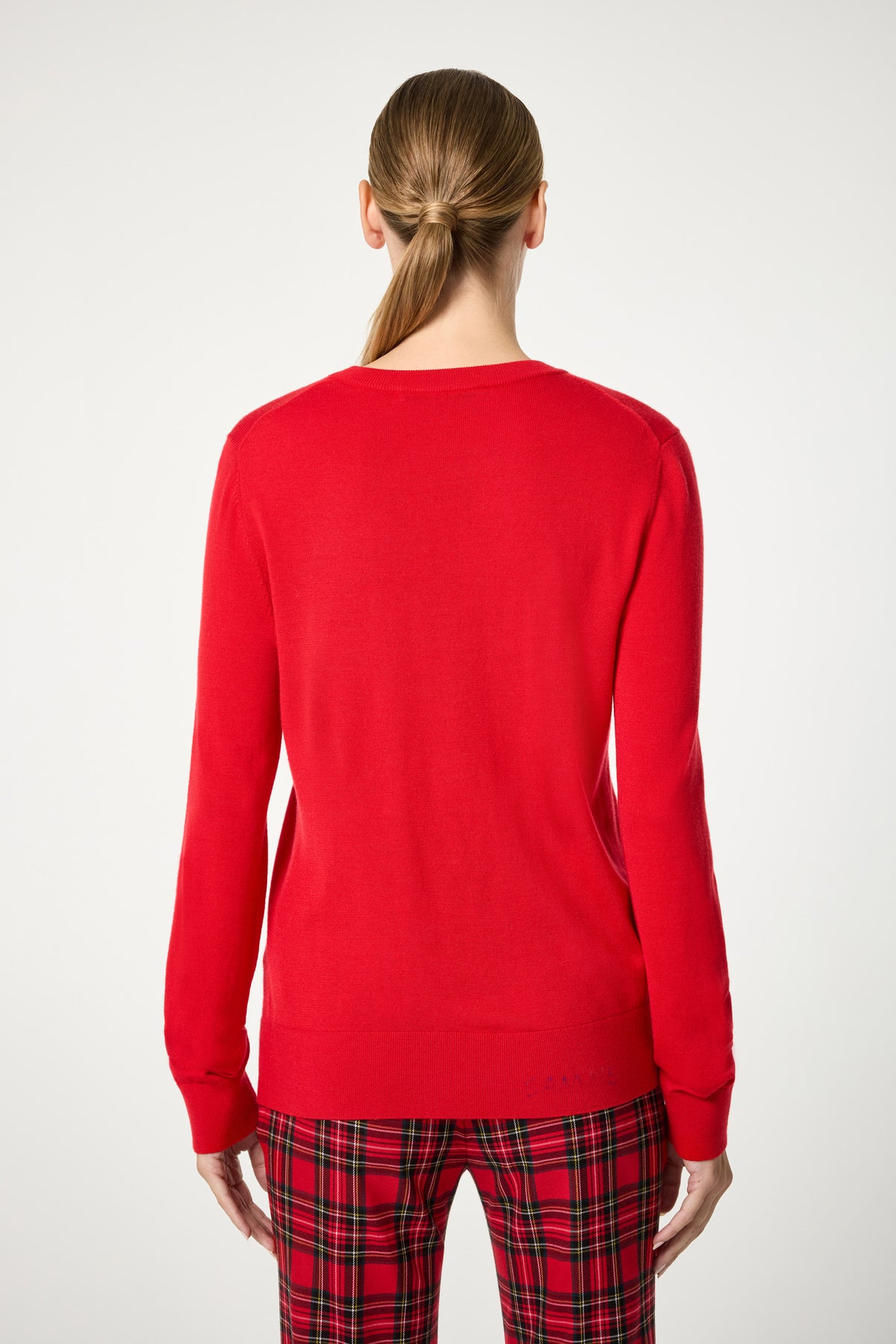 A woman with light brown hair in a low ponytail faces away, wearing the Jaguar Heart Crewneck Sweater in bright red, paired with red plaid pants against a plain white background.