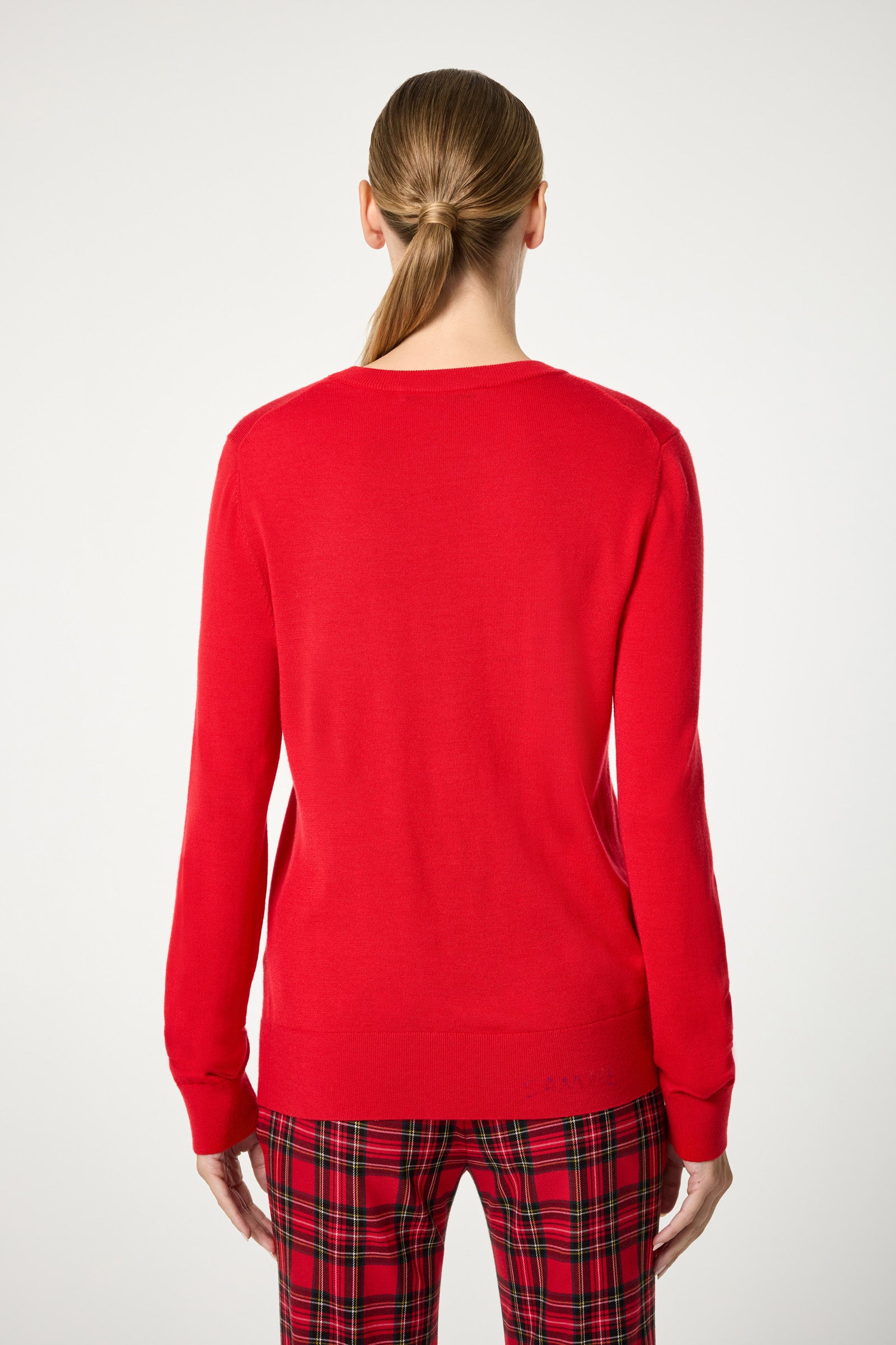 A woman with light brown hair in a low ponytail faces away, wearing the Jaguar Heart Crewneck Sweater in bright red, paired with red plaid pants against a plain white background.