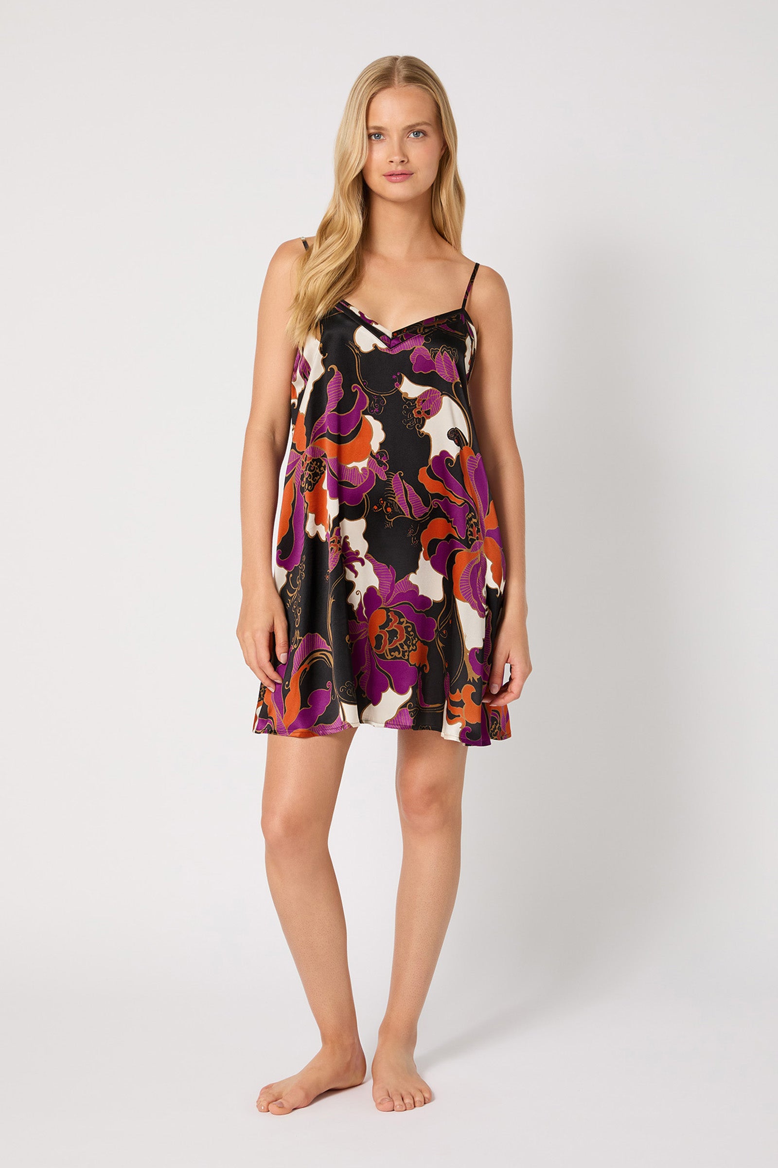 A woman stands barefoot against a plain white background, wearing the Silk Chemise Nightgown - Fall Floral, a sleeveless A-line slip dress with an abstract floral print in black, pink, orange, and purple.