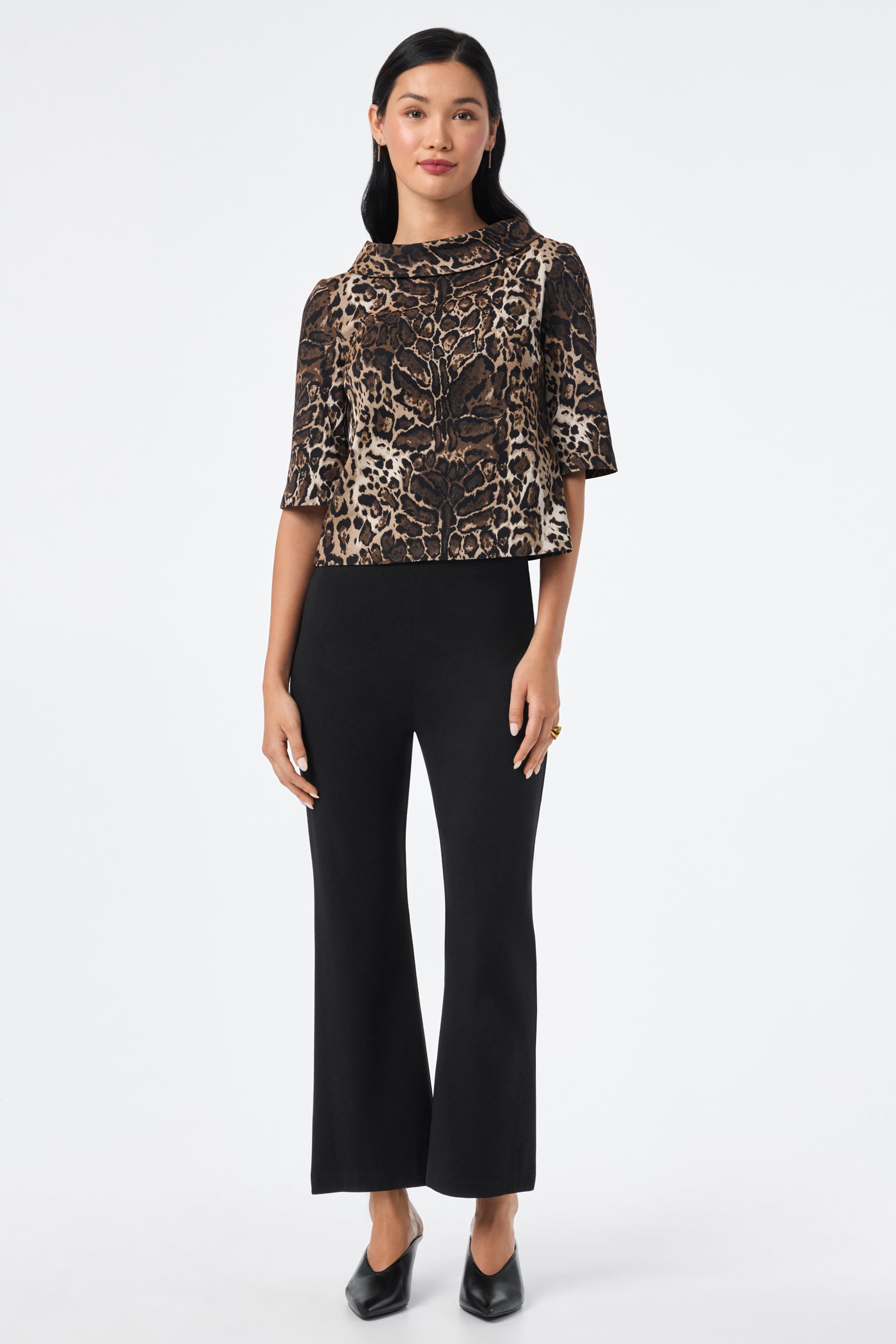 A woman faces forward against a plain white background, wearing the Kailee Top in brown leopard print, paired with black wide-leg pants and black pointed shoes.