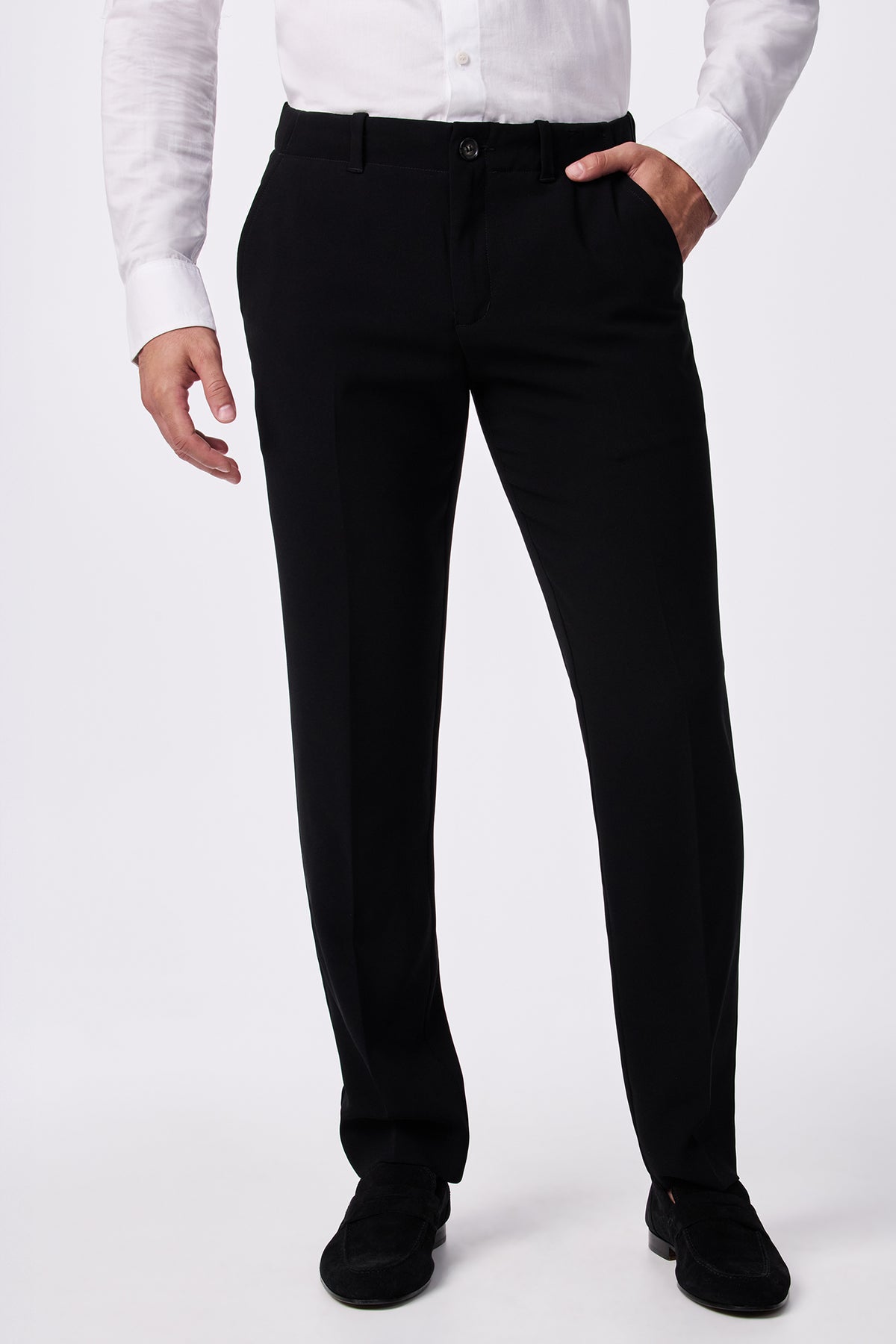 A person wearing the Alex Slim Trouser - Drapey Suiting in black, paired with a white long-sleeve shirt and black shoes, stands with one hand in their pocket against a plain white background.