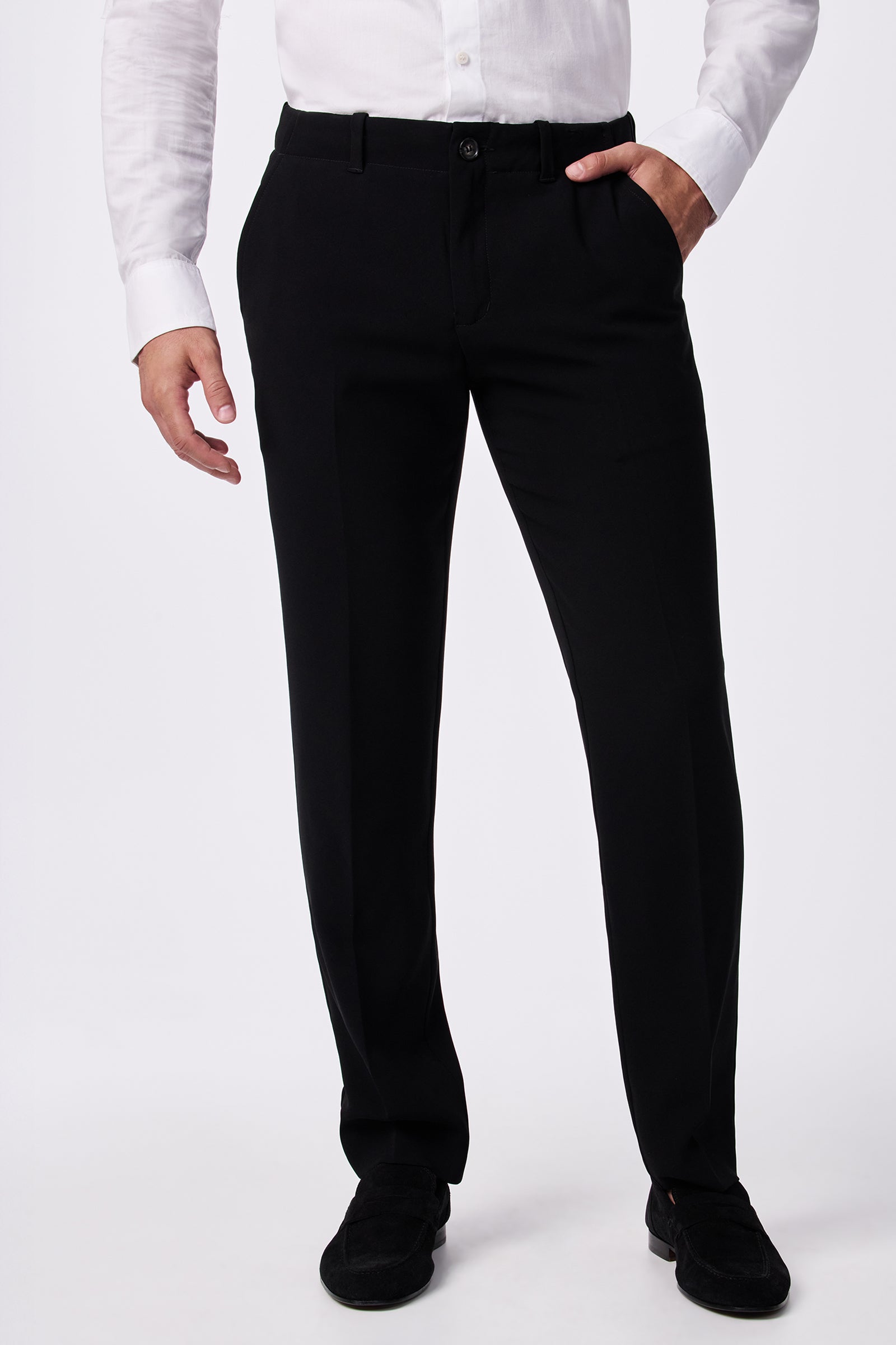 A person wearing the Alex Slim Trouser - Drapey Suiting in black, paired with a white long-sleeve shirt and black shoes, stands with one hand in their pocket against a plain white background.