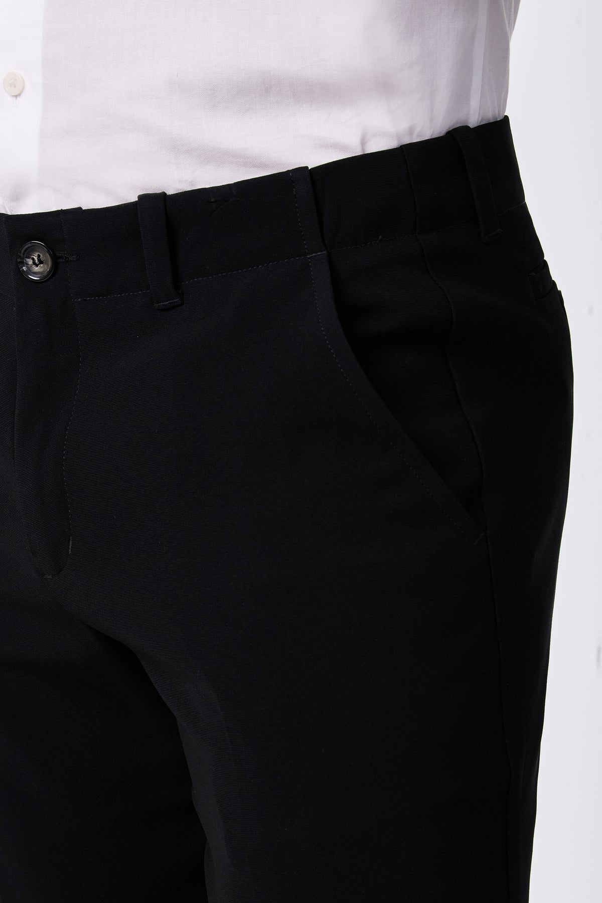 A person wearing the Alex Slim Trouser - Drapey Suiting in black with a white shirt, shown from waist to mid-thigh, one hand in the trouser pocket.