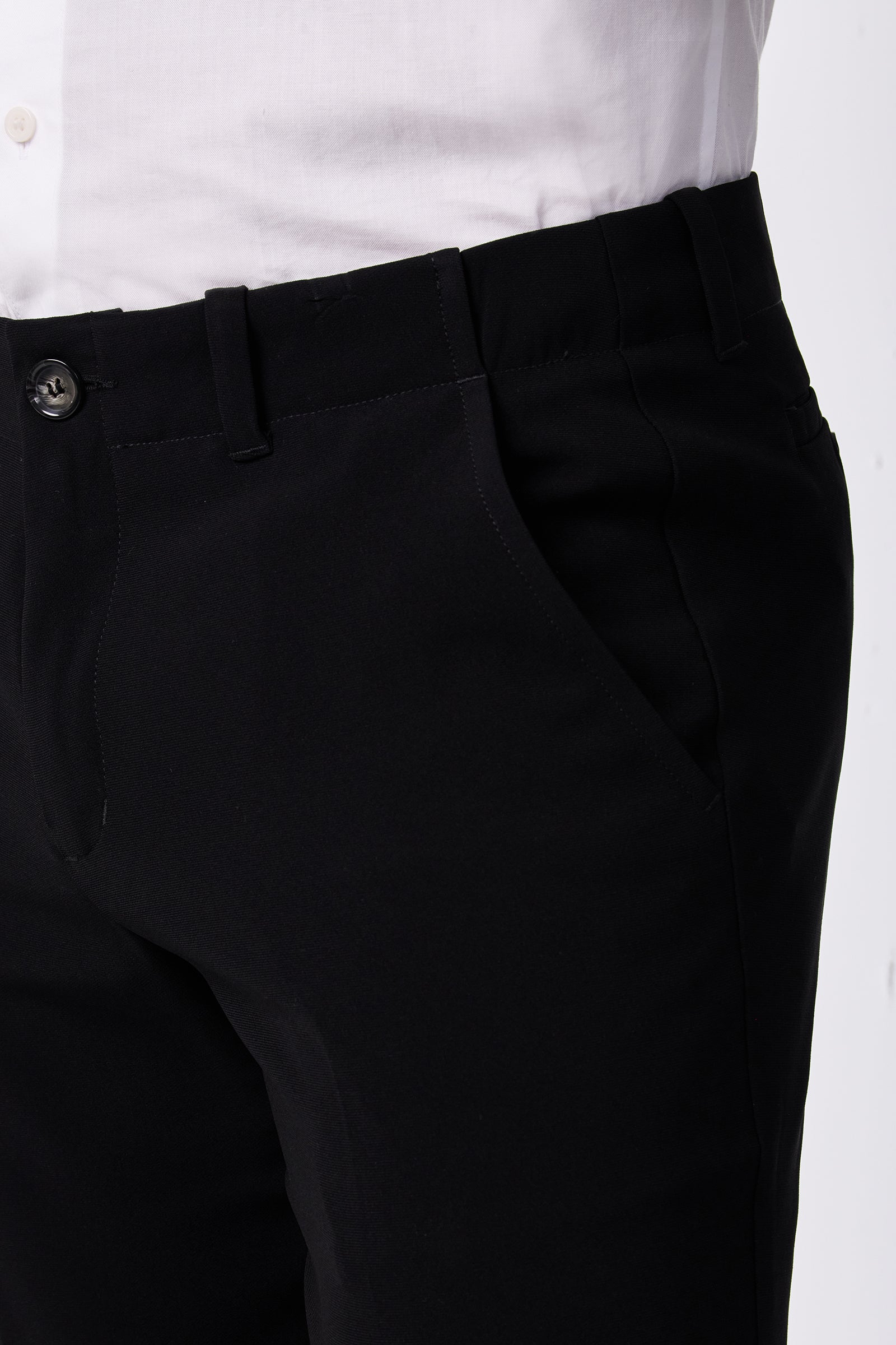 A person wearing the Alex Slim Trouser - Drapey Suiting in black with a white shirt, shown from waist to mid-thigh, one hand in the trouser pocket.