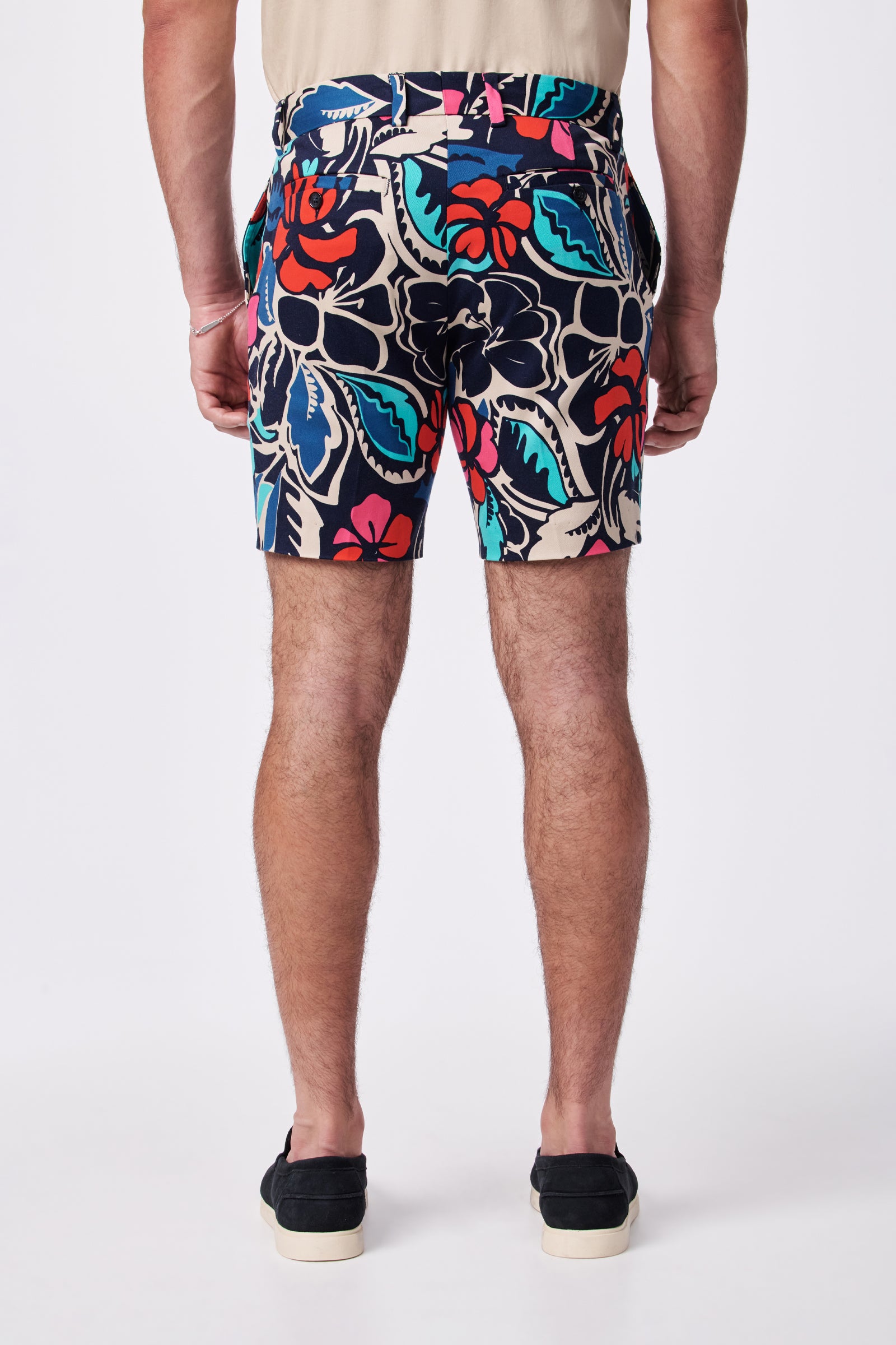 A person faces away, wearing the Lawrence Short featuring a colorful floral pattern in red, blue, teal, and cream, paired with black slip-on shoes against a plain white background.