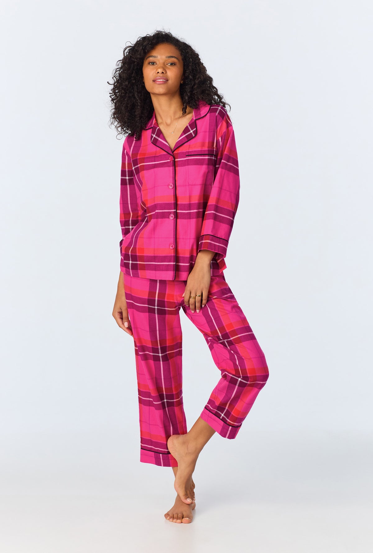 A woman poses barefoot against a light background, wearing the Aurora Plaid Womens 3/4-Sleeve Cropped Pant Flannel PJ Set in multi, featuring a button-up top with 3/4 sleeves and matching cropped pants.