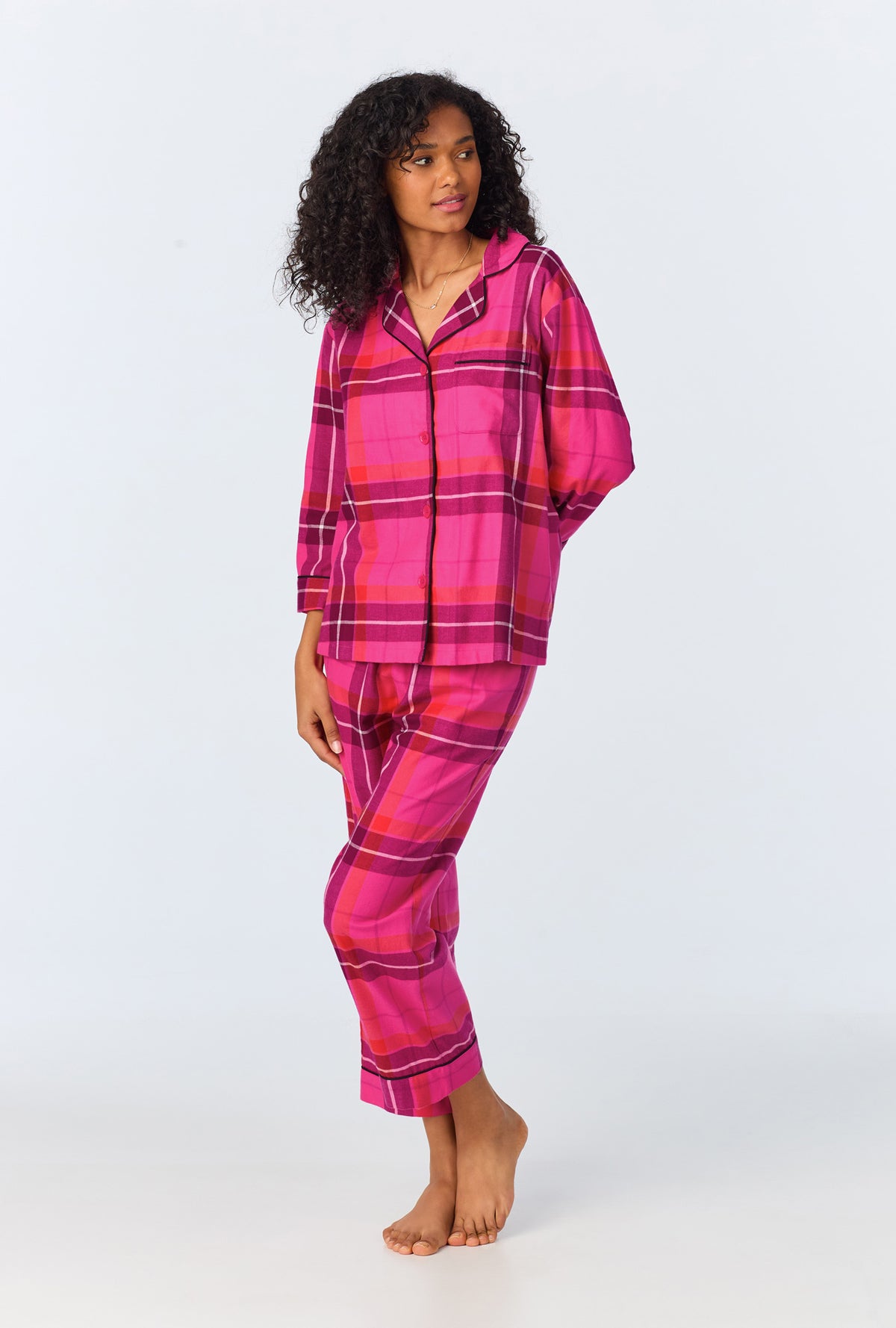 A woman stands barefoot against a light background wearing the Aurora Plaid Womens 3/4-Sleeve Cropped Pant Flannel PJ Set, looking off to the side.