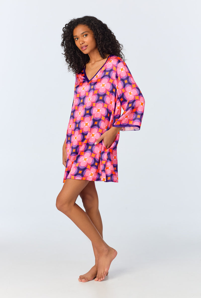 A woman with curly hair stands barefoot in a loose Space Cat Womens 3/4-Length Sleeve Silk Caftan. She poses with one hand in her pocket against a plain light background.