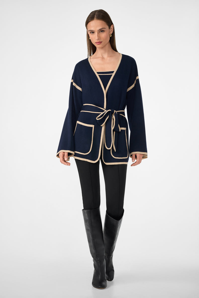 A woman wears the Casady Knit Cami, paired with a navy cardigan featuring beige trim and a belt, black leggings, and black knee-high boots. She stands facing forward against a plain light background.