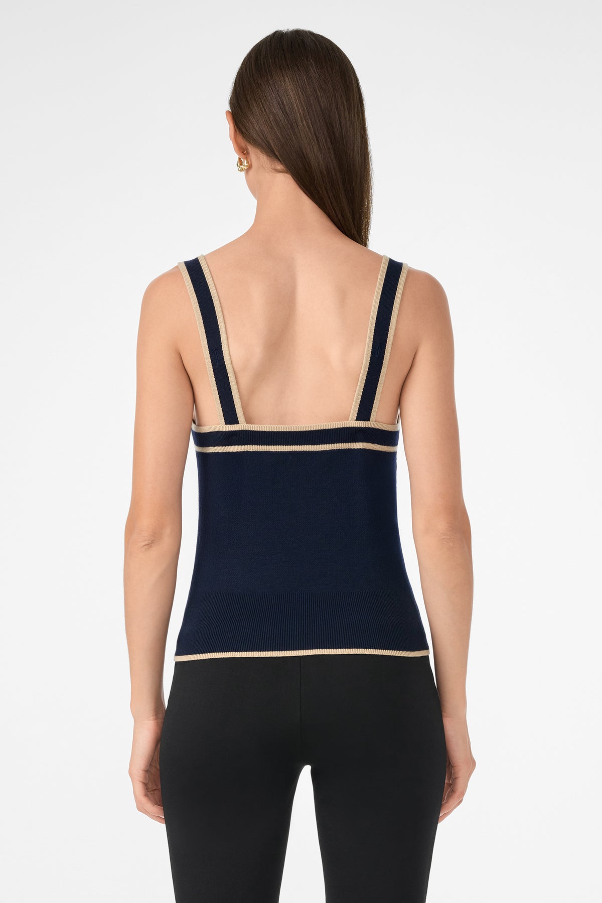 A woman with long brown hair is shown from the back wearing the Casady Knit Cami, a navy blue tank top with beige trim, paired with black leggings against a plain white background.