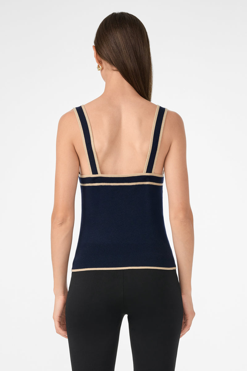 A woman with long brown hair is shown from the back wearing the Casady Knit Cami, a navy blue tank top with beige trim, paired with black leggings against a plain white background.