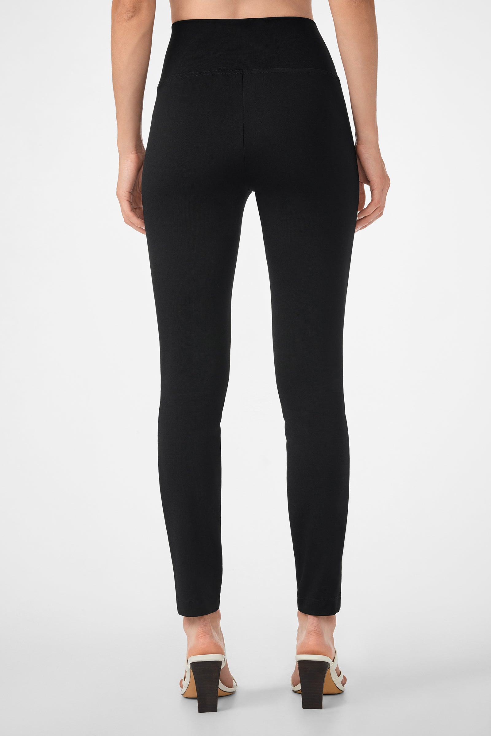 Someone is shown from the back wearing the high-waisted, fitted black Rose Pant and white heeled sandals, standing against a plain white background.