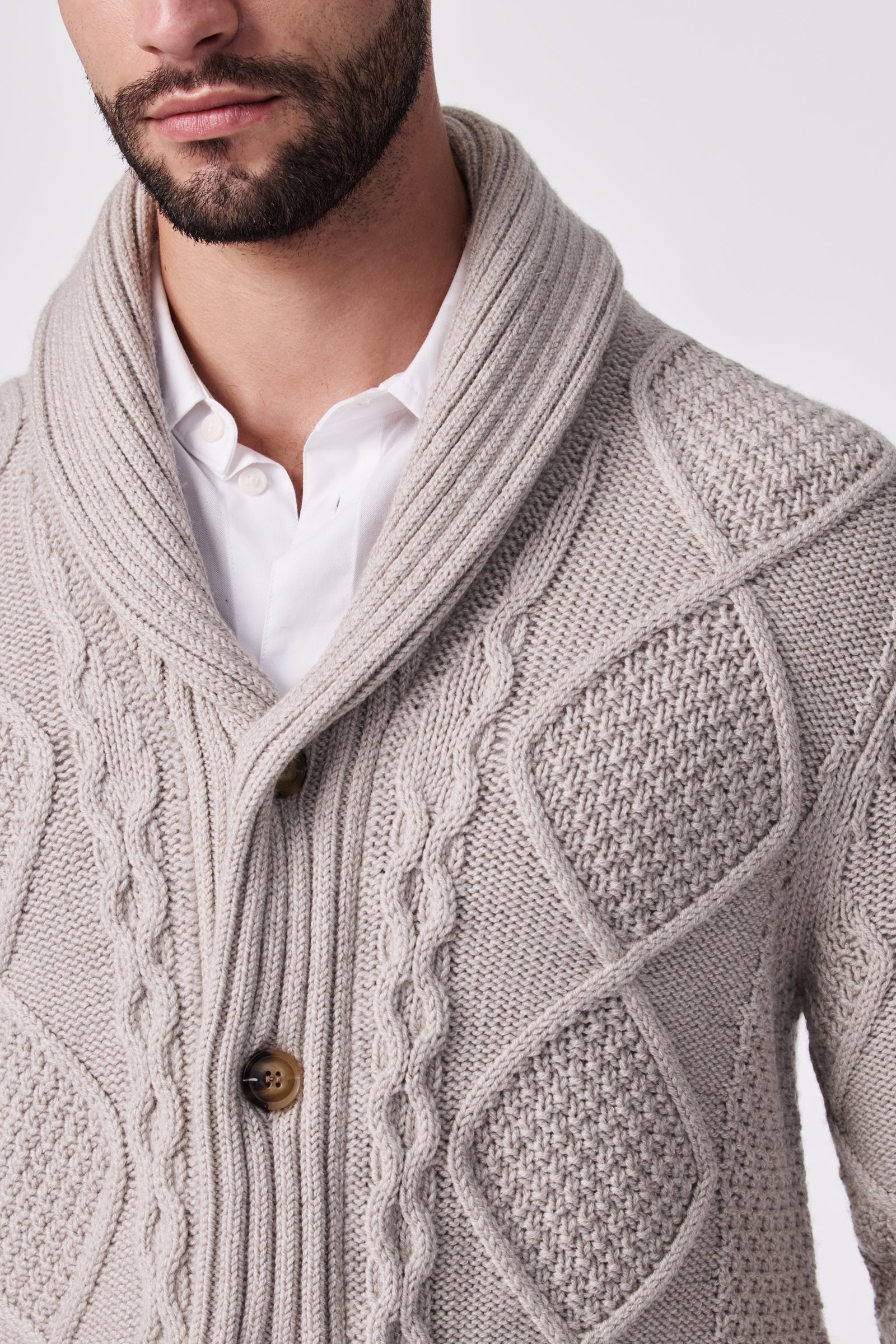 A man wearing the Brighton Cardigan, a light beige textured knit with a shawl collar and large buttons, layered over a white collared shirt. Only his lower face and upper torso are visible.
