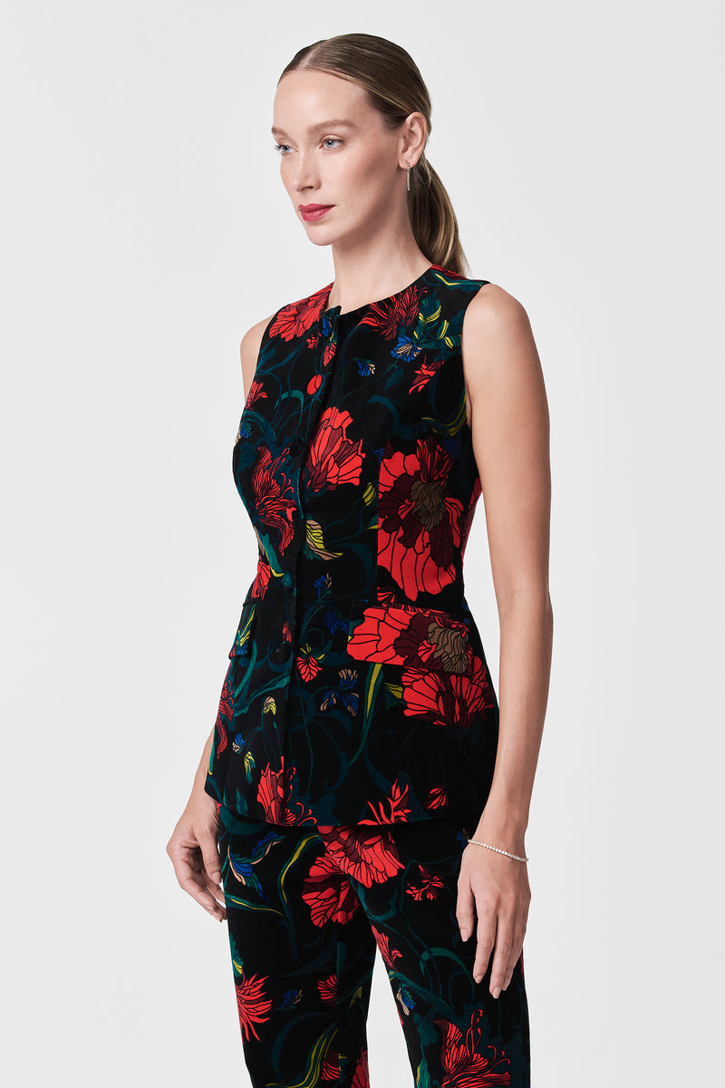 A woman with light skin and straight, pulled-back hair wears the Kary Printed Velvet Vest and matching pants in a bold red and blue floral pattern, standing against a plain white background.