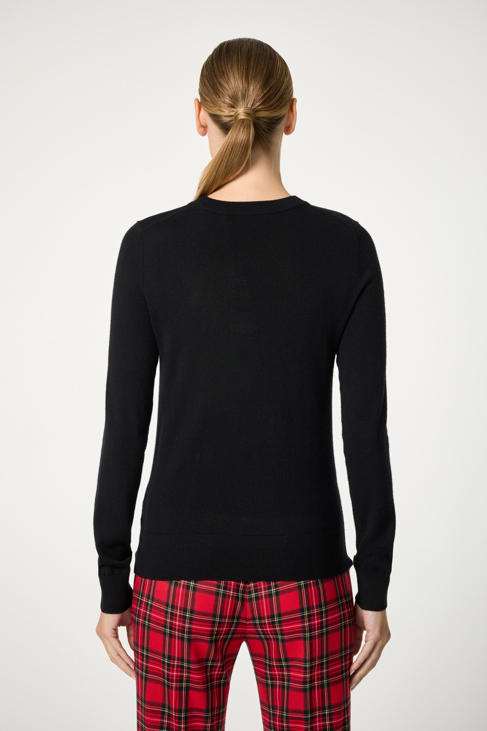 A person with long, straight hair in a low ponytail, seen from the back, wears the Plaid Heart Crewneck Sweater against a plain light background.