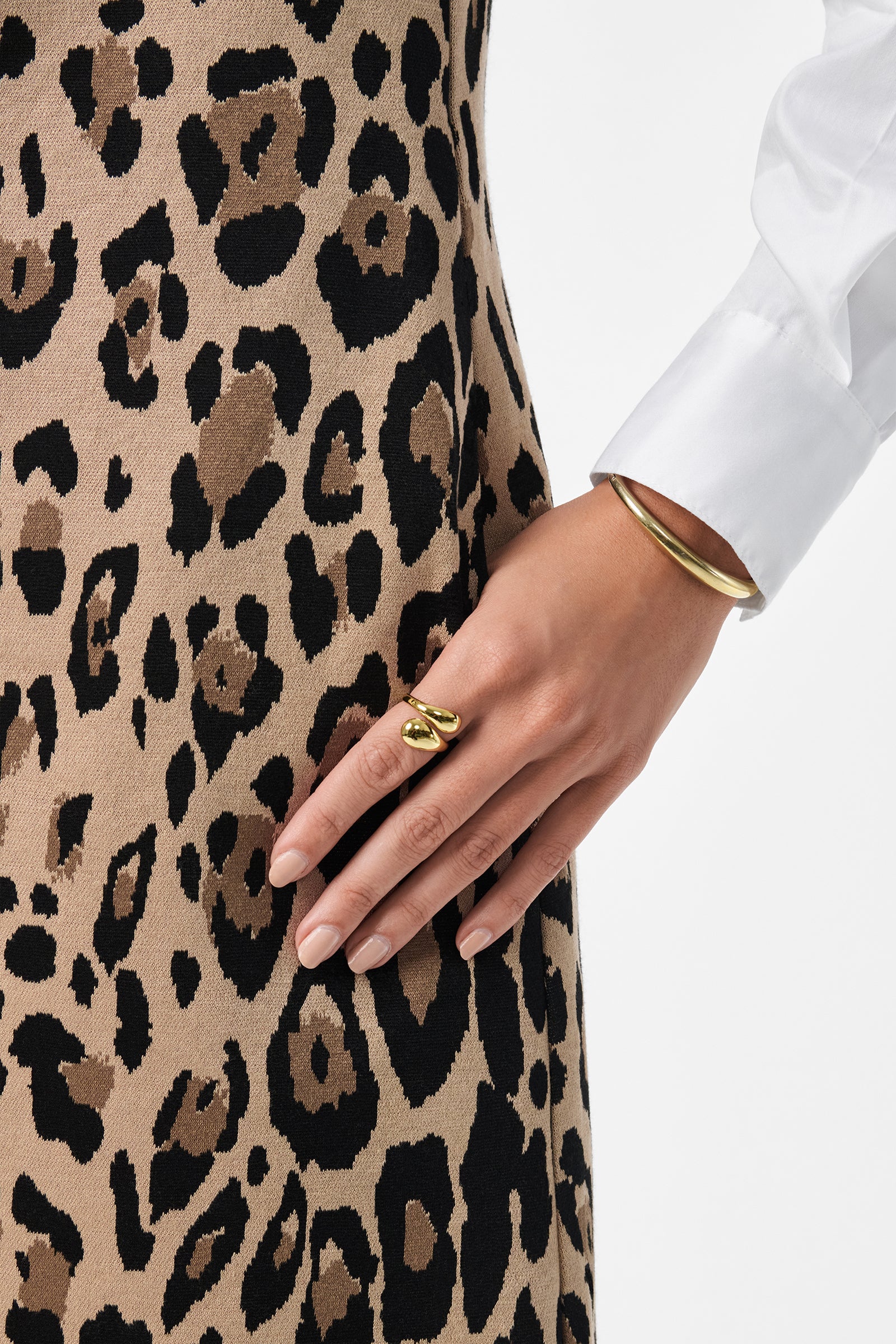 A close-up of a hand with gold jewelry resting on a tan and black leopard print Adapted Dress, paired with a white long-sleeve shirt.