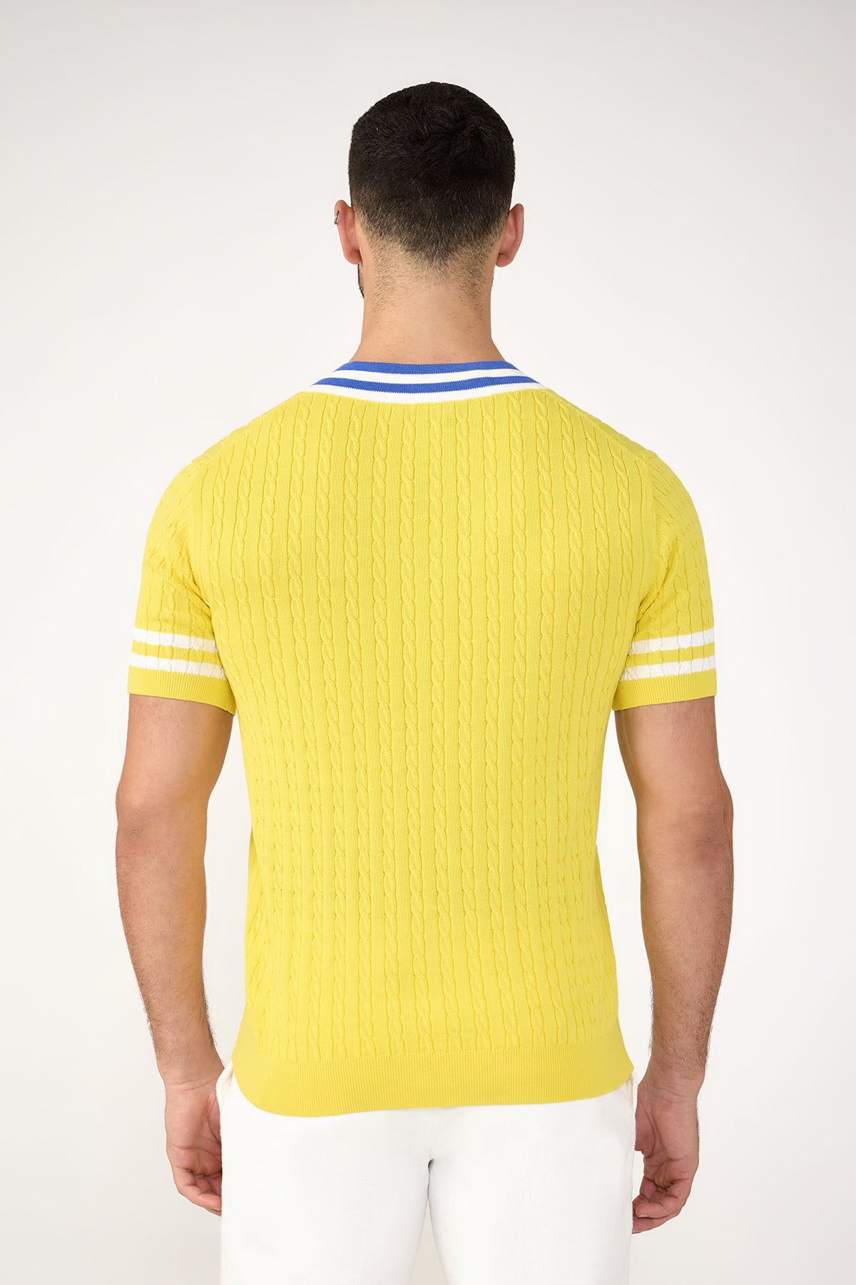 A man with short dark hair stands facing away, wearing the Ferguson Short-Sleeve V-Neck in yellow with white sleeve stripes and a blue-and-white striped collar, paired with white pants against a plain light background.