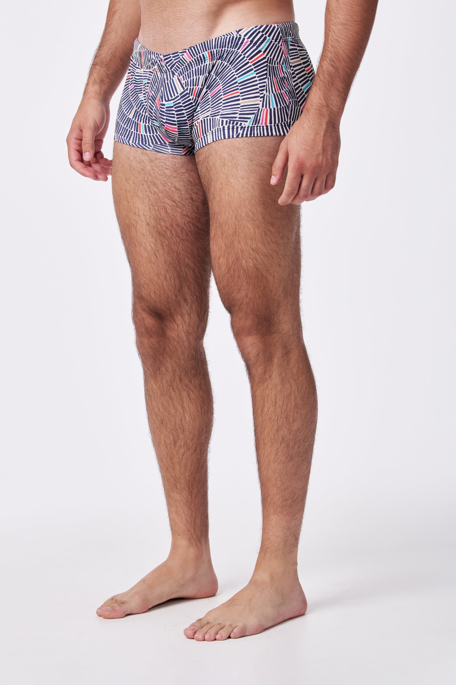 A man stands barefoot wearing Sorrento Swim Trunk featuring a blue, white, and red geometric pattern, shown from mid-torso to feet against a plain white background.