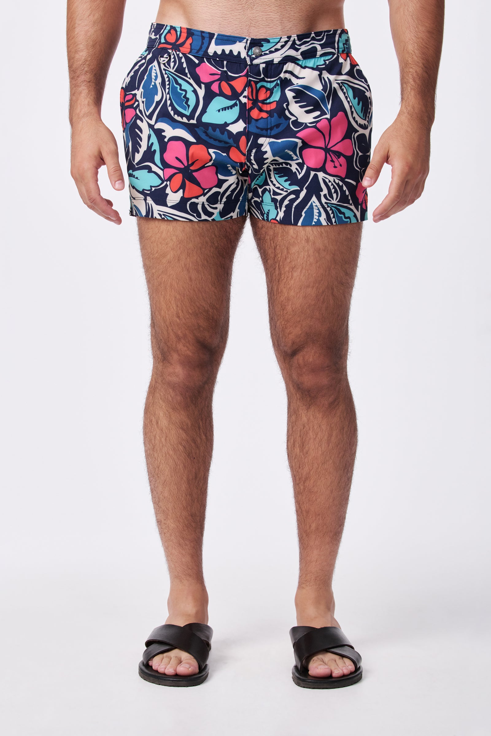 A person is shown from the waist down against a white background, wearing Chico Swim Trunk - Copacabana with a colorful, floral pattern and black slide sandals.