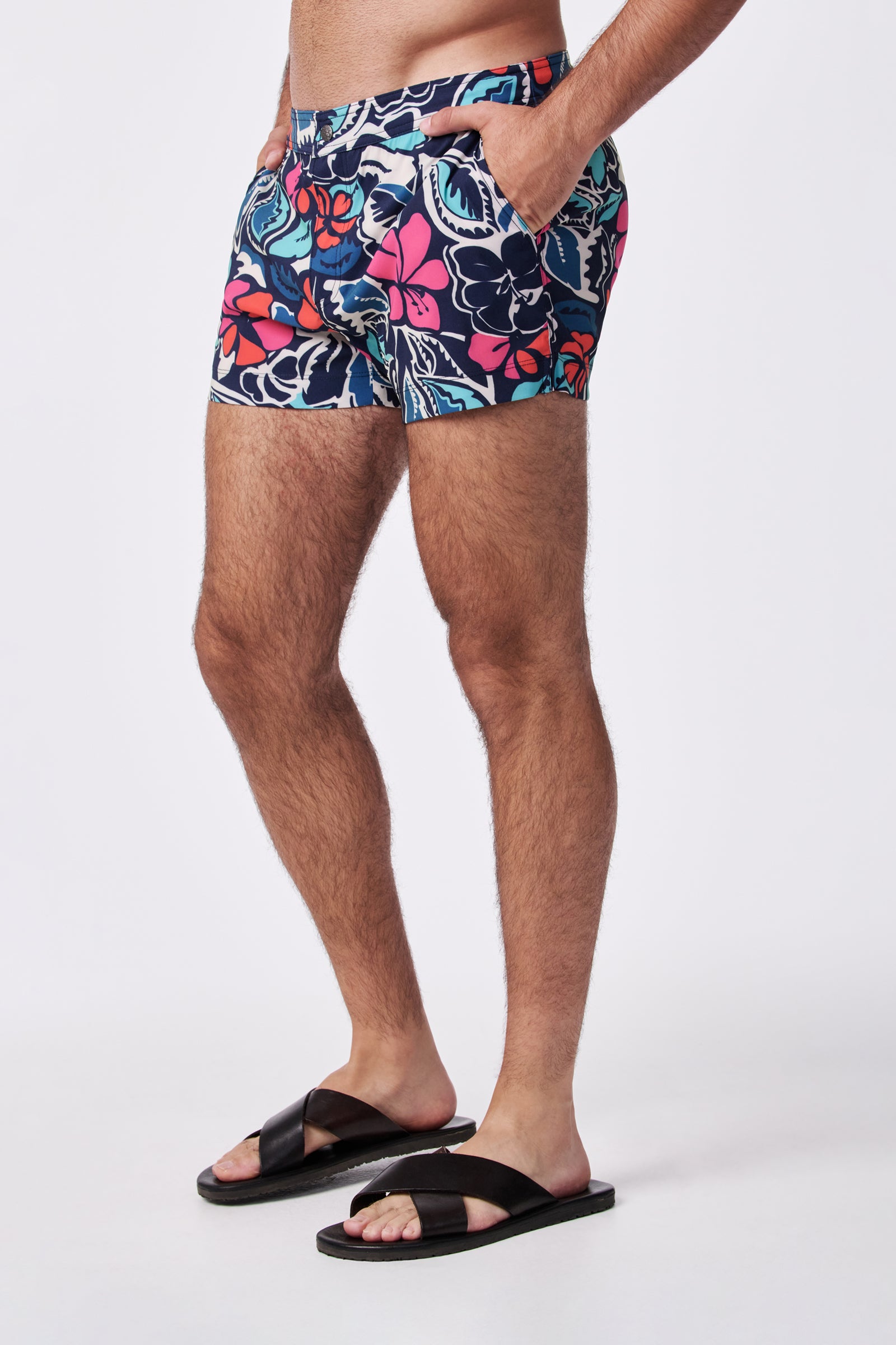 Wearing Chico Swim Trunk - Copacabana and black slide sandals, a person stands with hands in pockets, shown from mid-chest to feet against a plain white background.