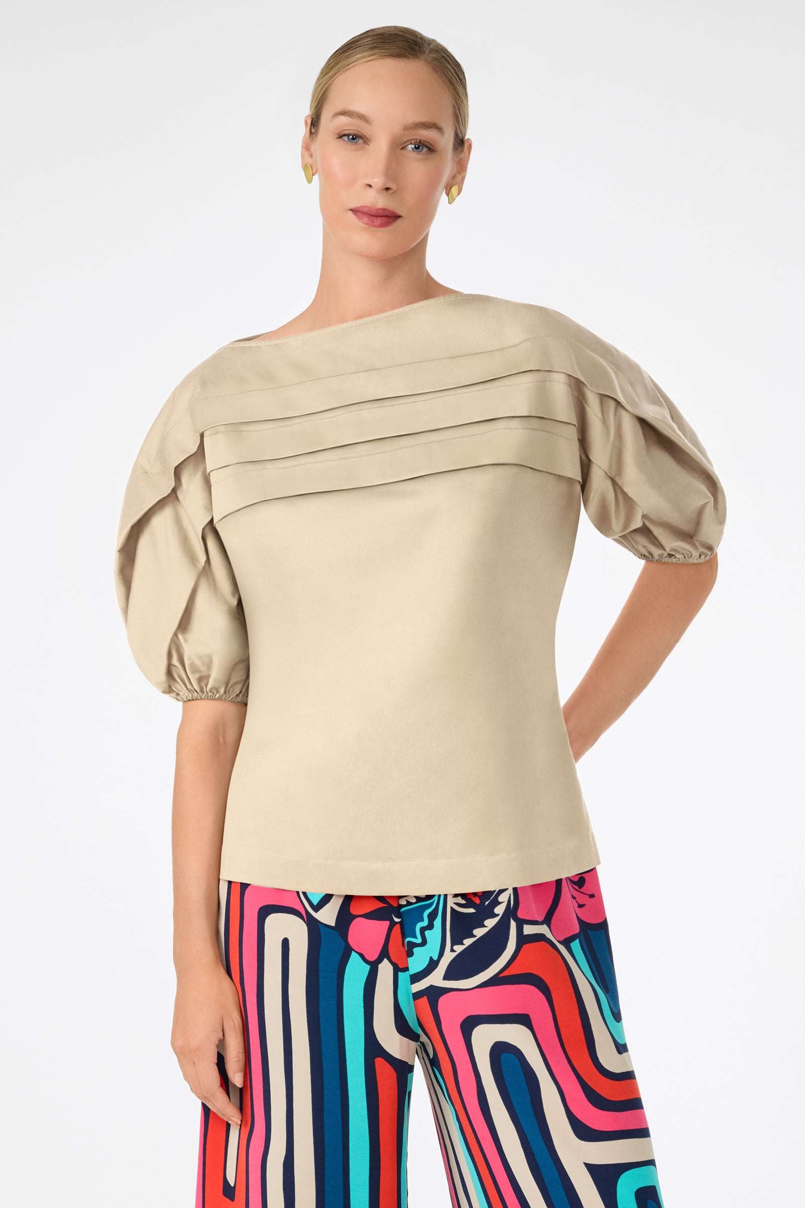 A woman wearing the Grady Puff-Sleeve Top in beige and colorful, abstract-patterned pants stands against a plain white background, looking at the camera with a relaxed expression.