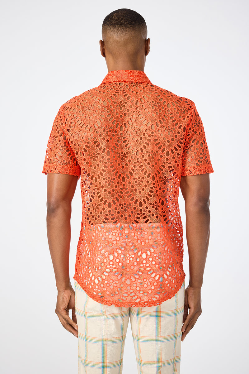 A person stands facing away, wearing the Long Beach Short-Sleeve Shirt in bright orange with a see-through lace pattern and light-colored plaid pants, set against a plain white background.